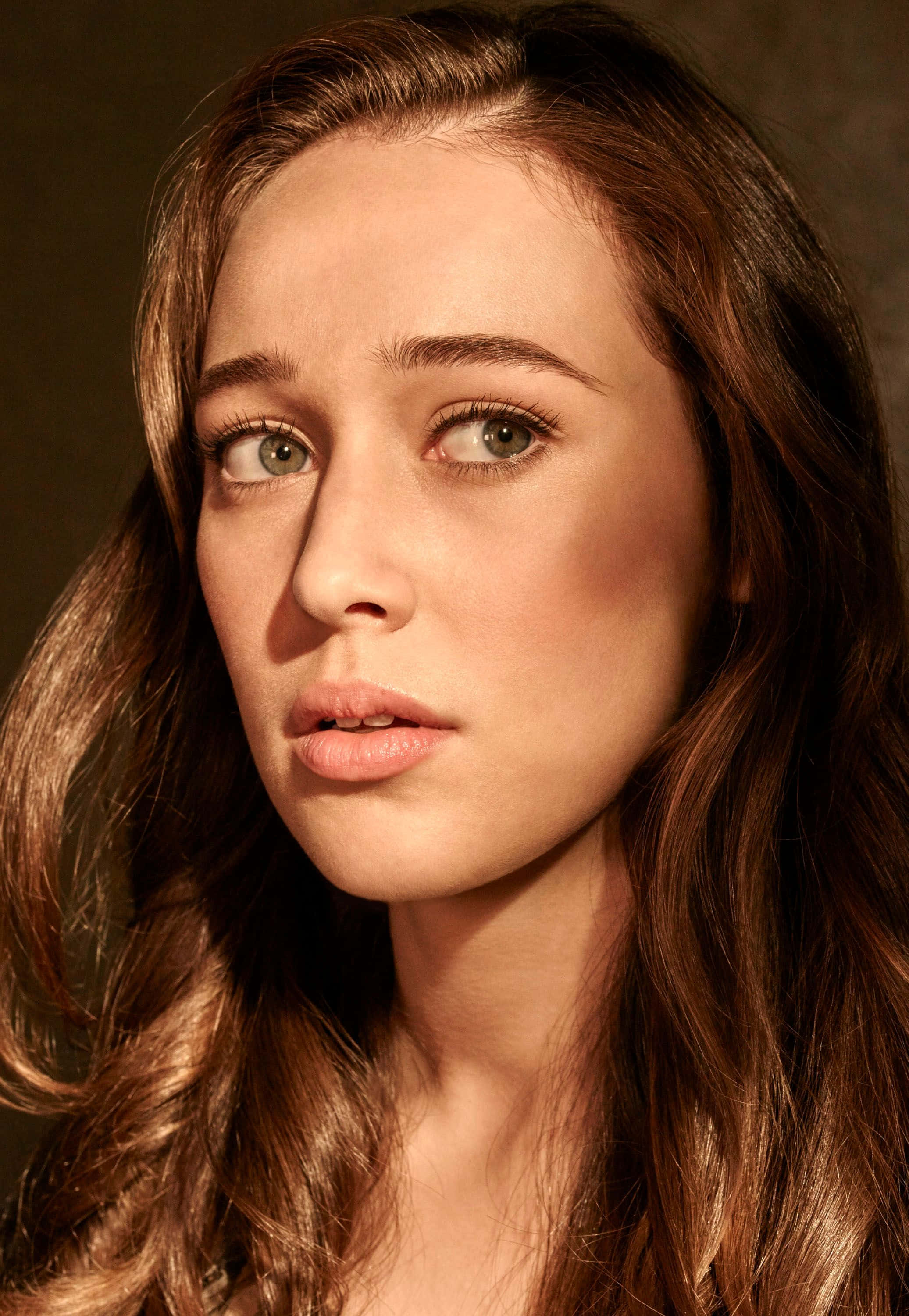 alycia debnam carey 桌布 壁紙 — 一位年輕女性的特寫肖像，擁有長長的棕色頭髮和綠色眼睛，在溫暖的攝影棚燈光下若有所思地凝視鏡頭。