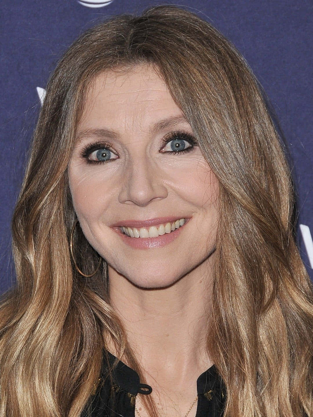 Sarah Chalke 桌布 壁紙 — 一個微笑女性的特寫肖像，擁有長波浪金髮和藍眼睛，背景為深藍色。