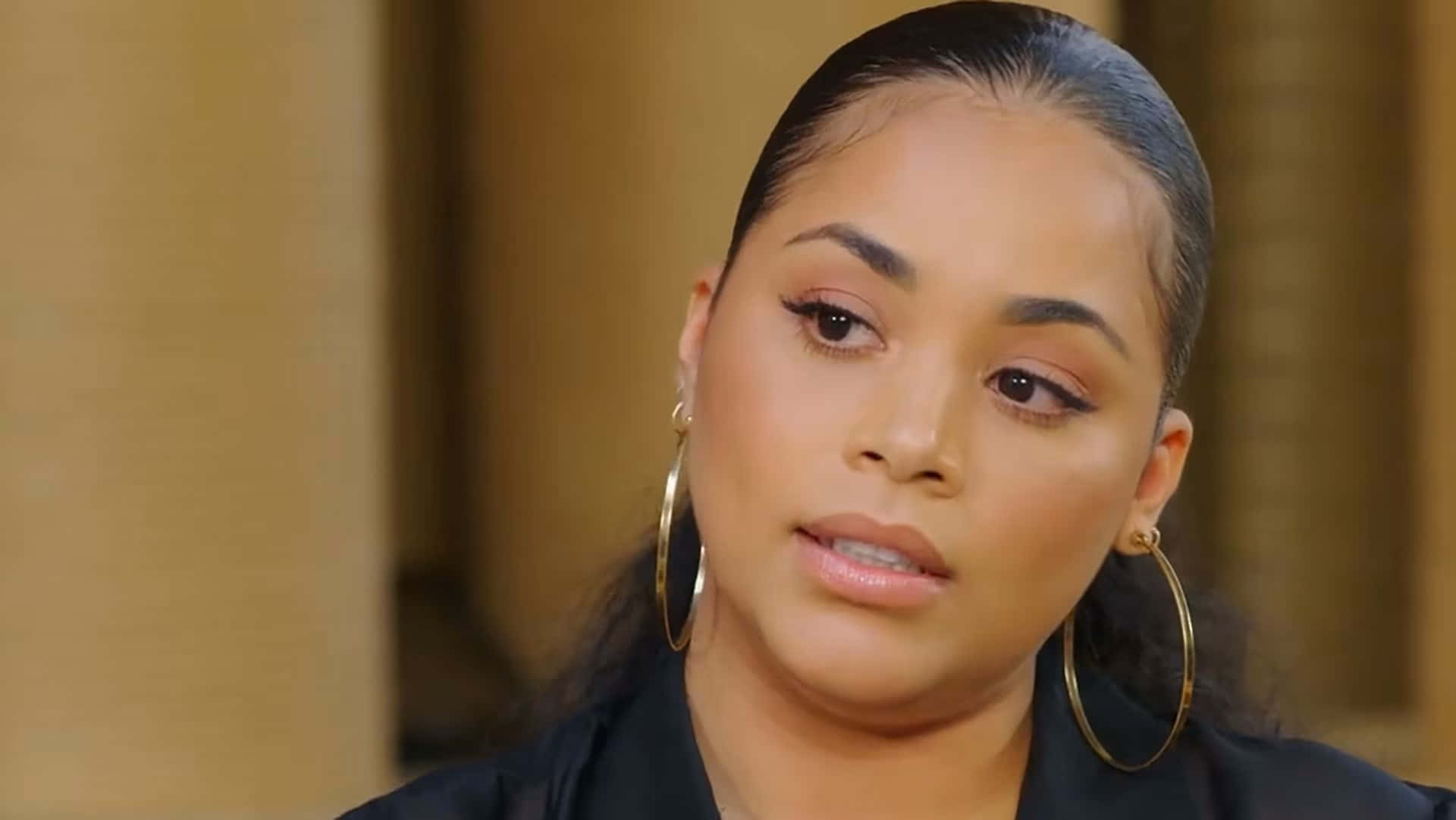Lauren London 桌布 壁紙 — 一位深色頭髮向後梳的女性特寫肖像，戴著大型金色圓環耳環和黑色上衣，背景溫暖模糊。