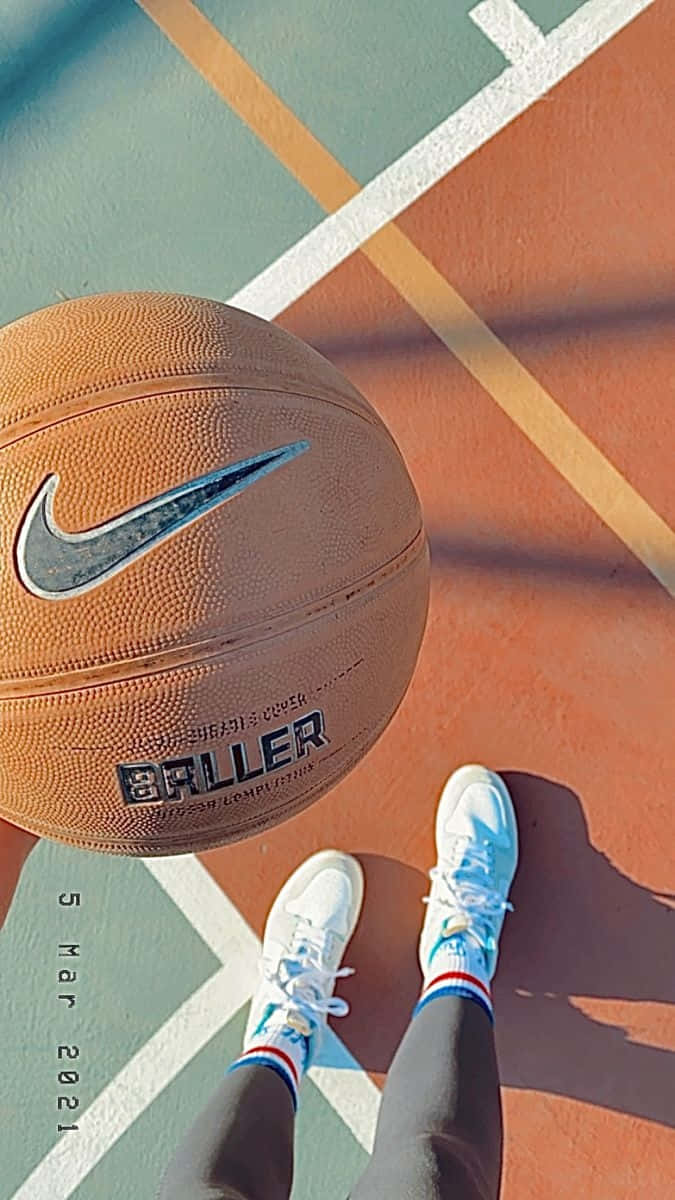  壁紙 — 一個近距離視角，顯示一個帶有Nike swoosh標誌的籃球放在色彩繽紛的球場上，旁邊是一個人的白色運動鞋。