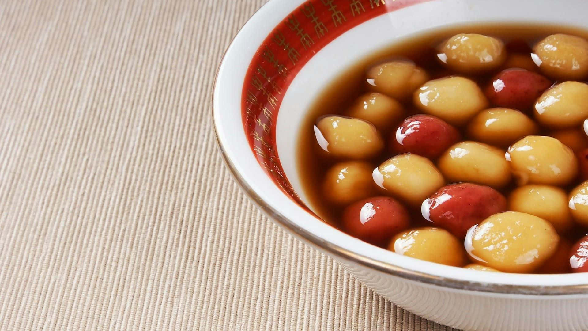  壁紙 — 一個白色陶瓷碗的特寫，碗邊有紅色圖案，裡面裝滿了閃亮的紅糖衣栗子和紅棗。