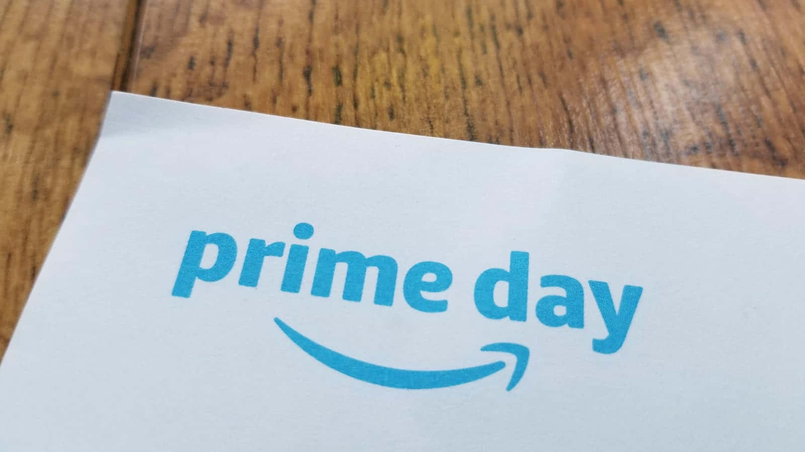 壁紙 — 白色紙張的特寫，上面有藍色「prime day」文字和箭頭標誌，放置在溫暖的木質表面上。