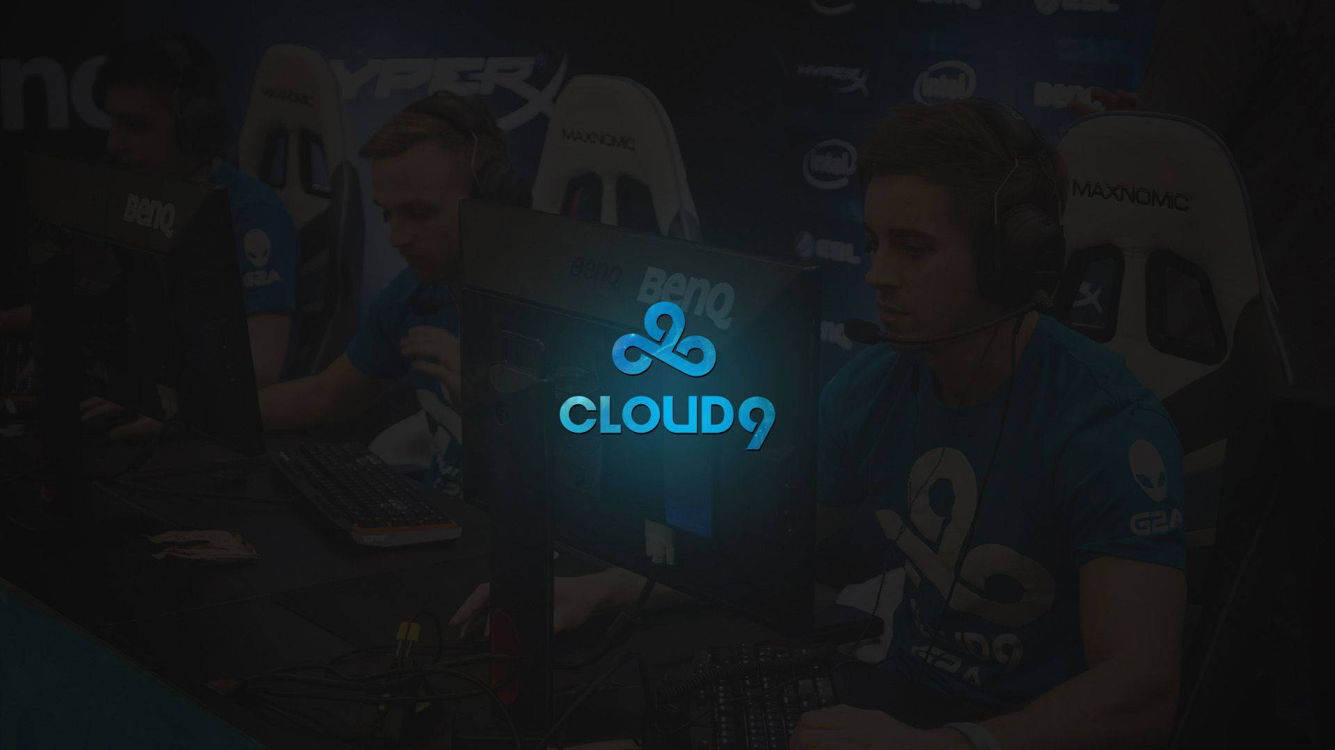Cloud9 標誌搭配電競選手 壁紙 — 專業電競選手在昏暗燈光下，於發光顯示器前全神貫注地參加比賽。