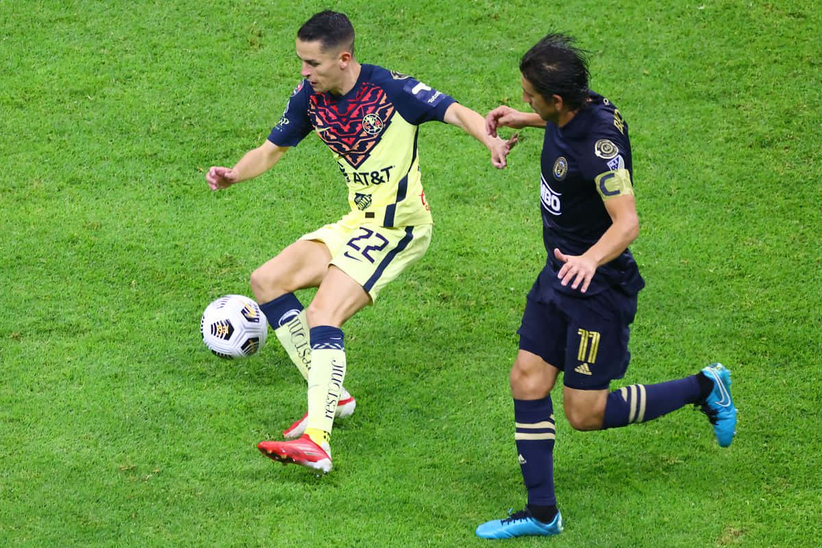 Club America 中場對決足球賽 壁紙 — 兩名足球運動員在體育場燈光下，於充滿活力的綠色草地上激烈爭奪球權。