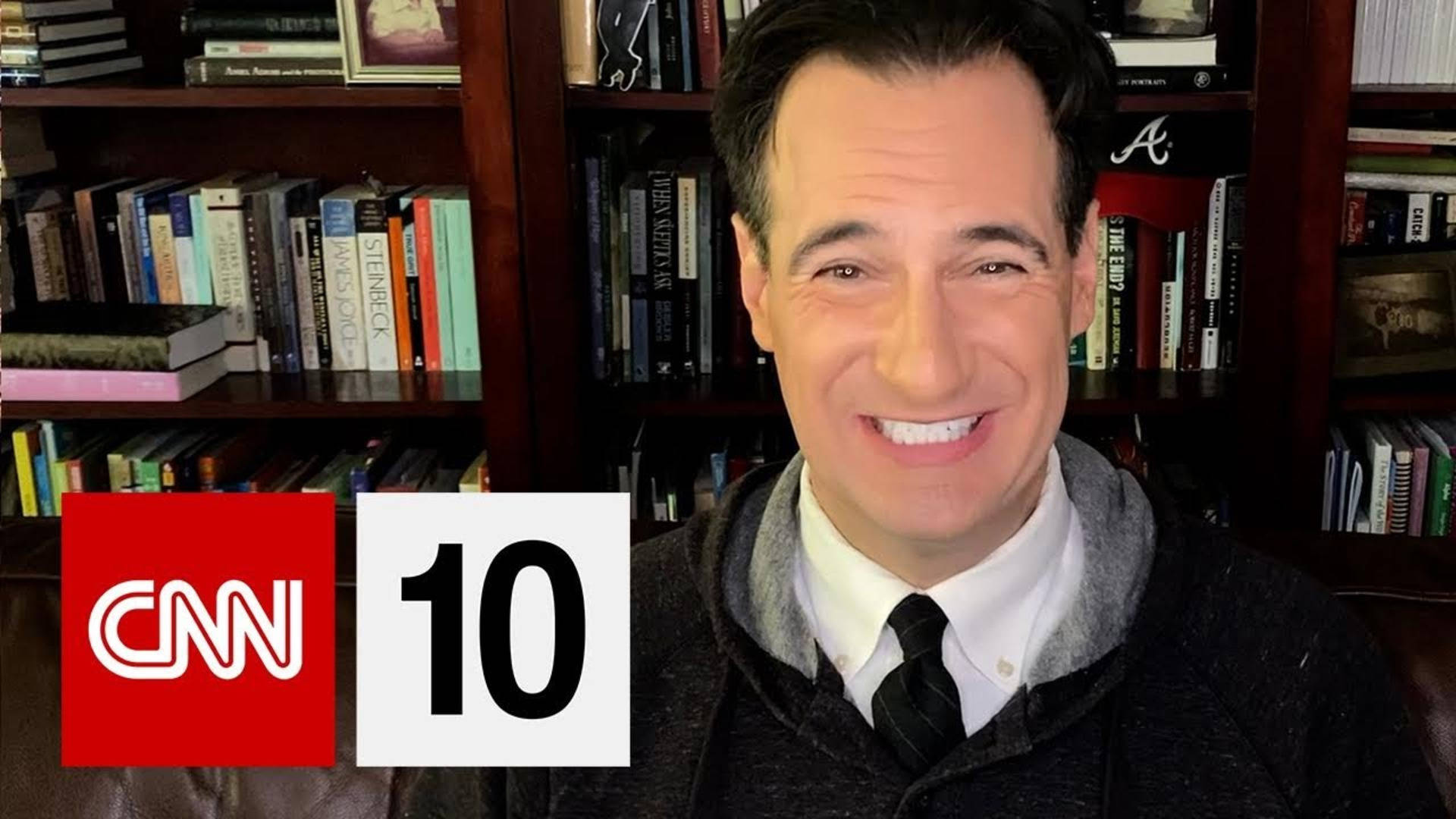 微笑男子在顯示CNN 10標誌的書架前。