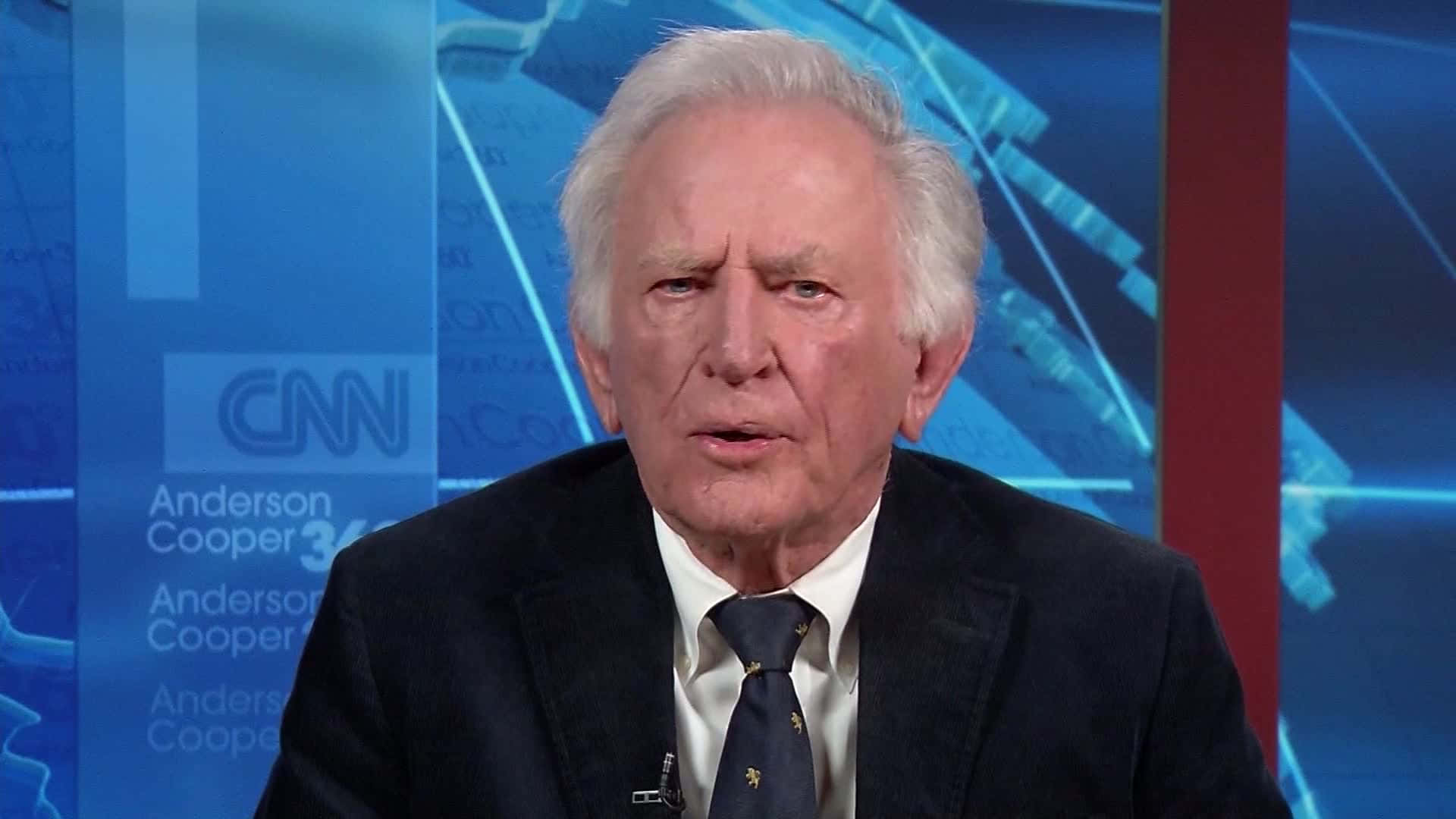 加里·哈特接受CNN訪問 壁紙 — 安德森·庫珀在CNN上專注地說話，背後有藍色幾何圖形。