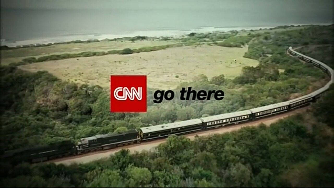 CNN Go There 非洲 壁紙 — 一列長長的火車蜿蜒穿過茂密的綠色森林，在陰天之下駛向遠方的大海。