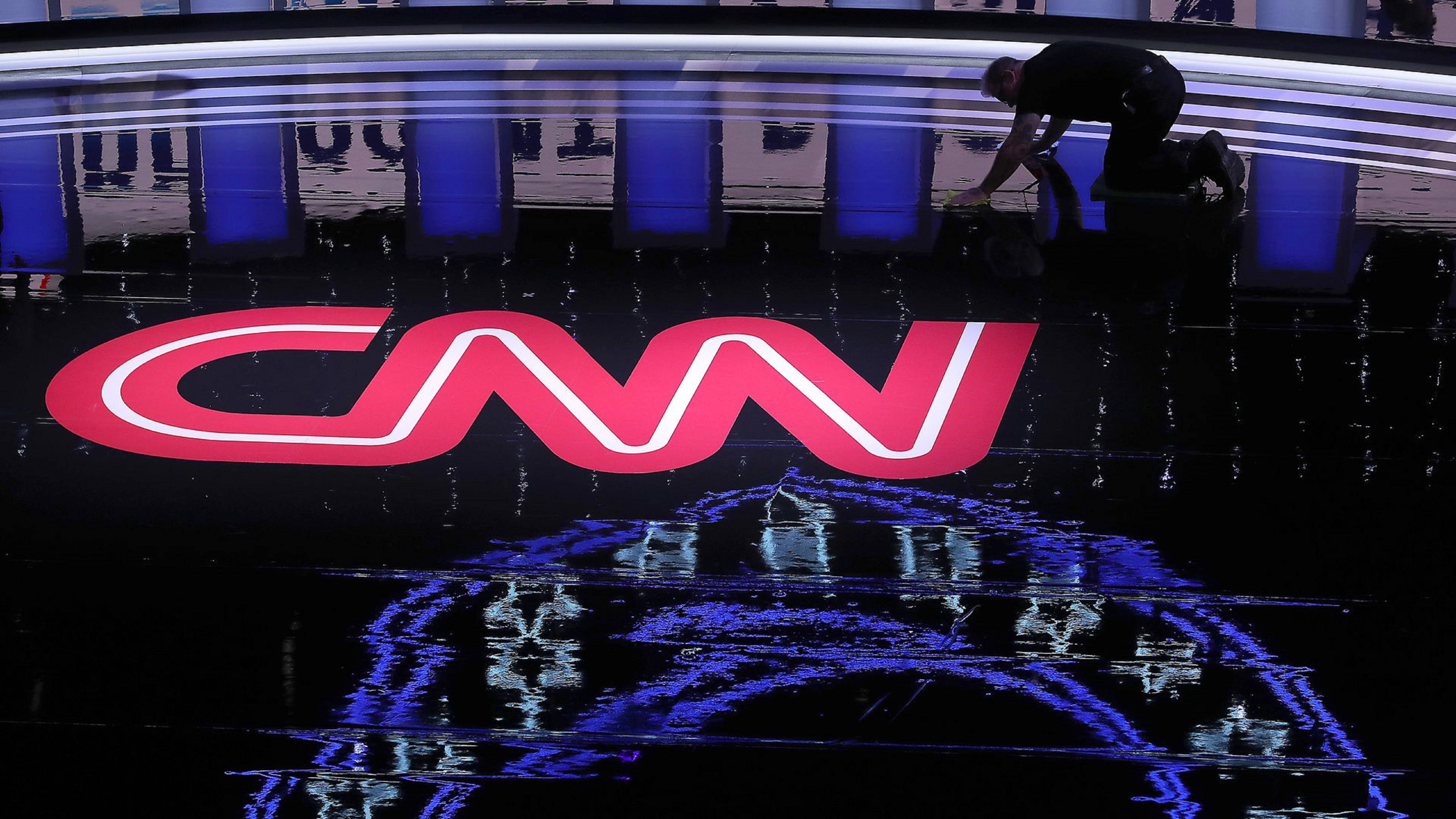 CNN 城市論壇 壁紙 — 一名工人跪在光亮的黑色地板上，反射出現代工作室中發光的紅色CNN標誌和藍色燈光。