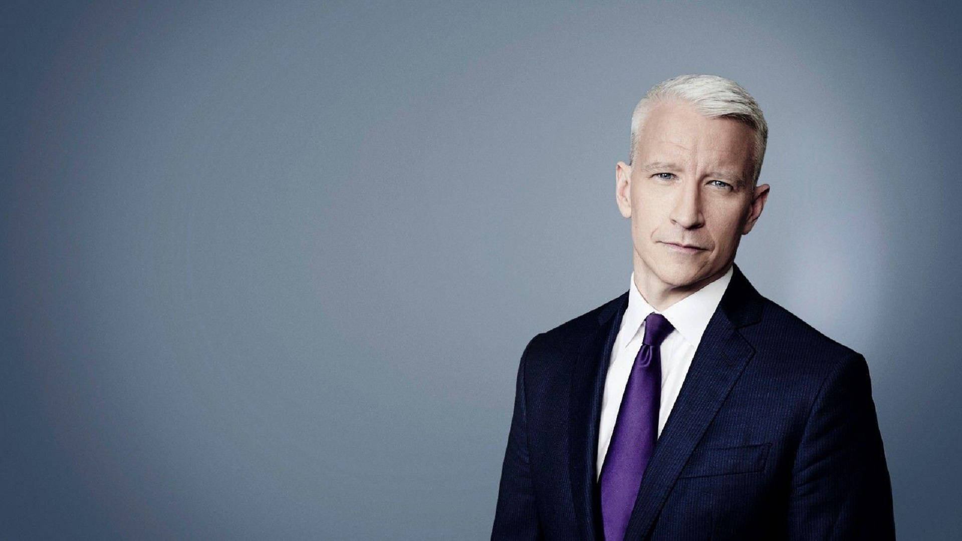 CNN 安德森·庫珀 壁紙 — 一位白髮男士穿著深色西裝和紫色領帶，背景是柔和的灰色攝影棚。