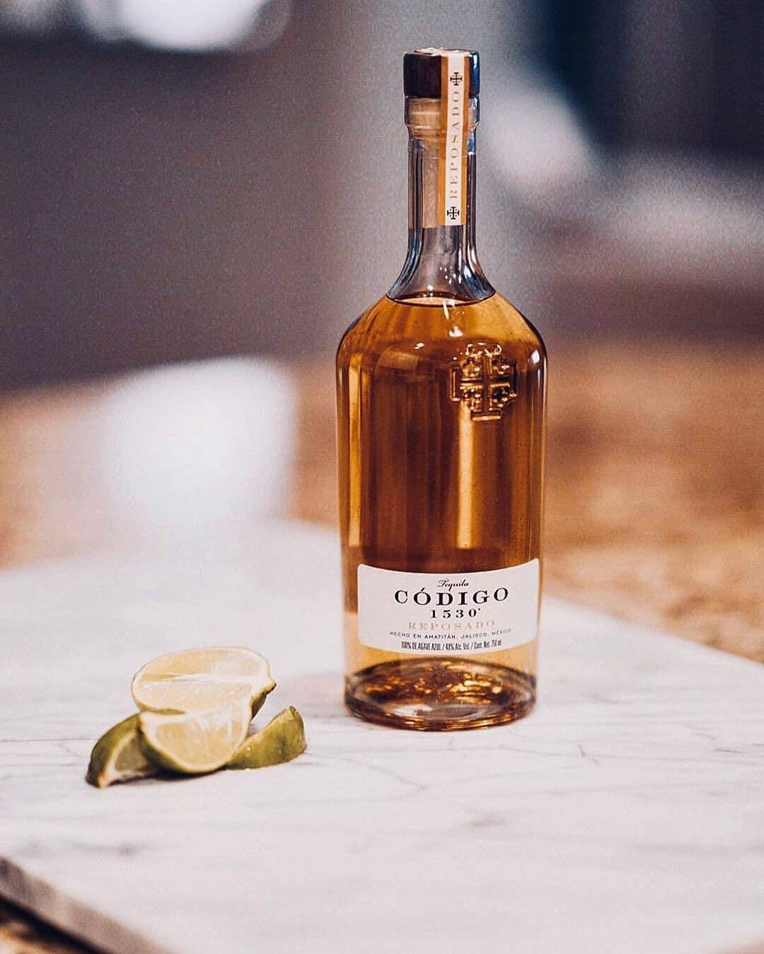 Codigo 1530 Reposado 酒瓶配切片檸檬 壁紙 — 一瓶 Código 1530 Reposado 龙舌兰酒优雅地放在大理石表面上，旁边是新鲜的青柠角。