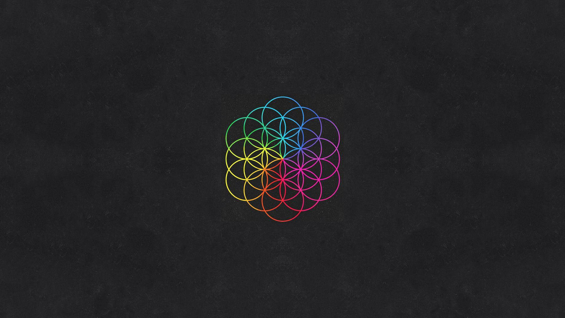 Coldplay幾何圖騰符號 壁紙 — 一個充滿活力的彩虹生命之花幾何圖案，居中在紋理深灰色背景上。