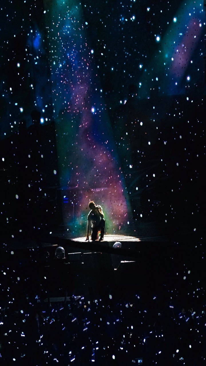 一對情侶在星光燦爛的宇宙燈光秀下在舞台上擁抱。