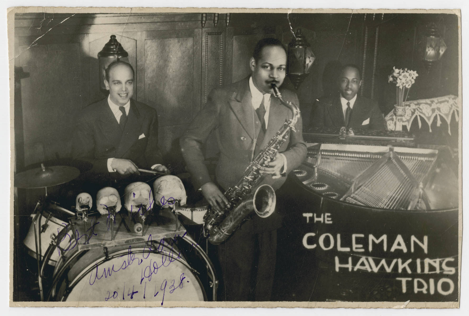 Coleman Hawkins 三重奏演出 壁紙 — Coleman Hawkins Trio 在燈光昏暗的爵士俱樂部中現場演奏色士風、鼓和鋼琴的復古黑白照片。