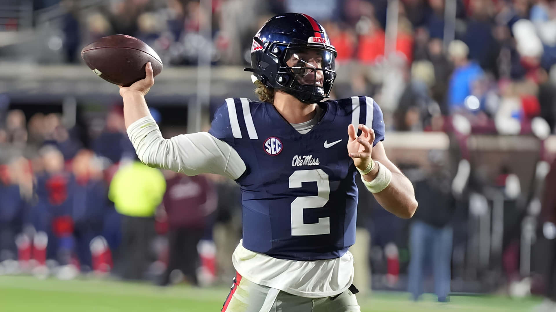  壁紙 — 一名大學美式足球四分衛身穿海軍藍 Ole Miss 球衣 2 號，在球場燈光下準備傳球。