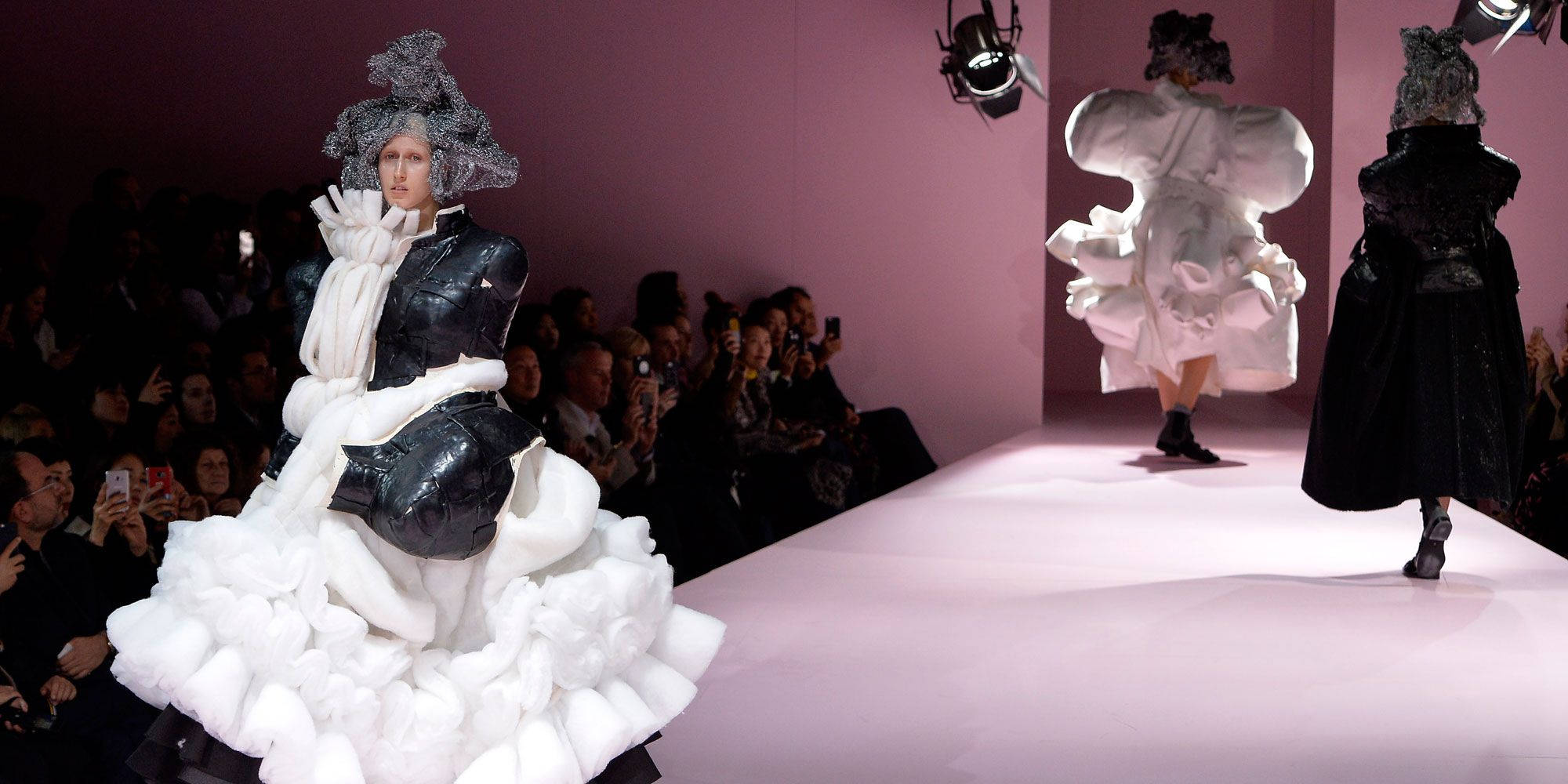 Comme Des Garçons 黑白高級時裝連衣裙 壁紙 — 模特兒在粉紅色天橋上走秀，穿著前衛的黑白服裝，帶有雕塑般的荷葉邊和戲劇性的頭飾。