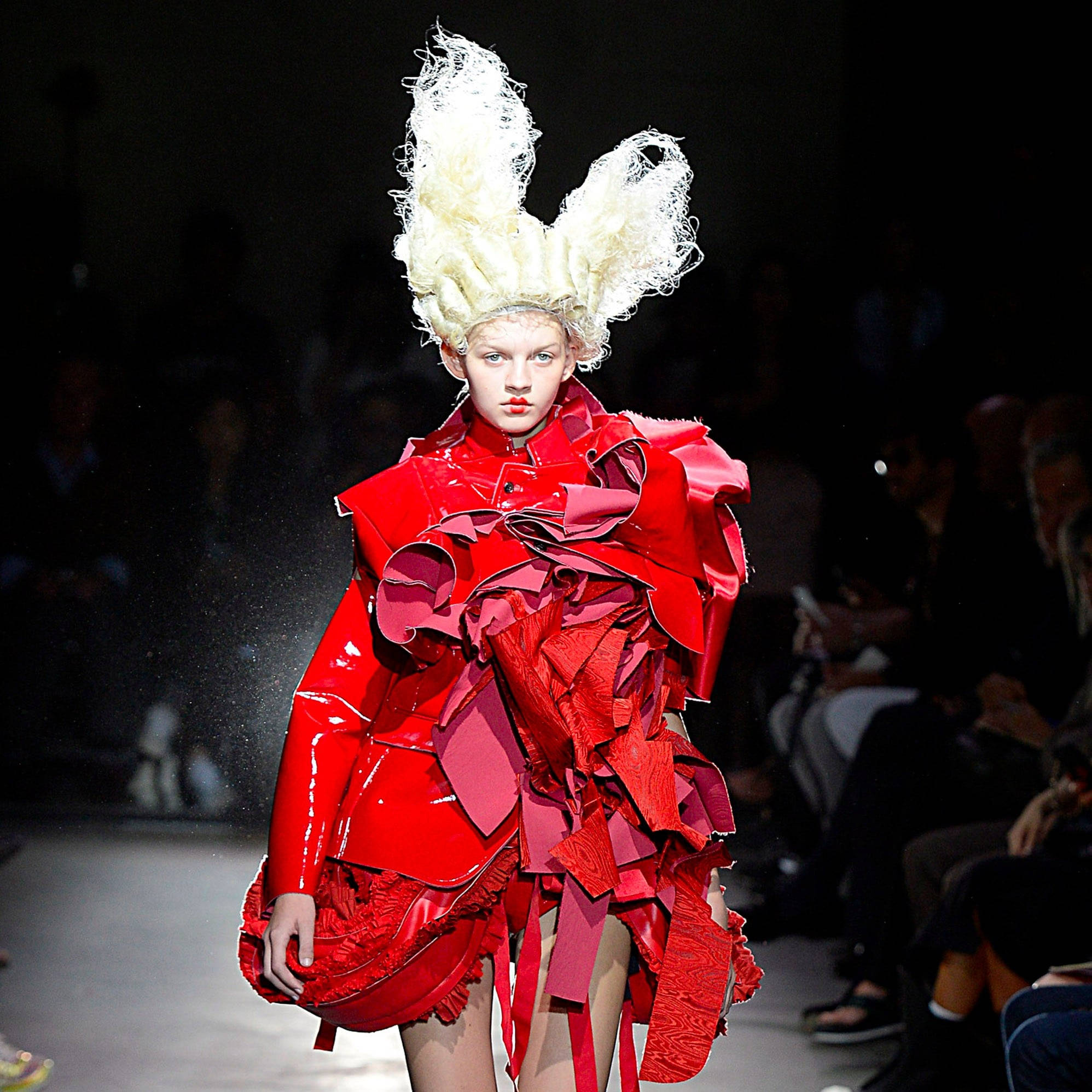 Comme Des Garçons 紅色乳膠禮服 壁紙 — 模特兒在戲劇性的舞台燈光下，穿著大膽的紅色分層服裝，配以高聳的白色頭飾，在時裝展台上走秀。