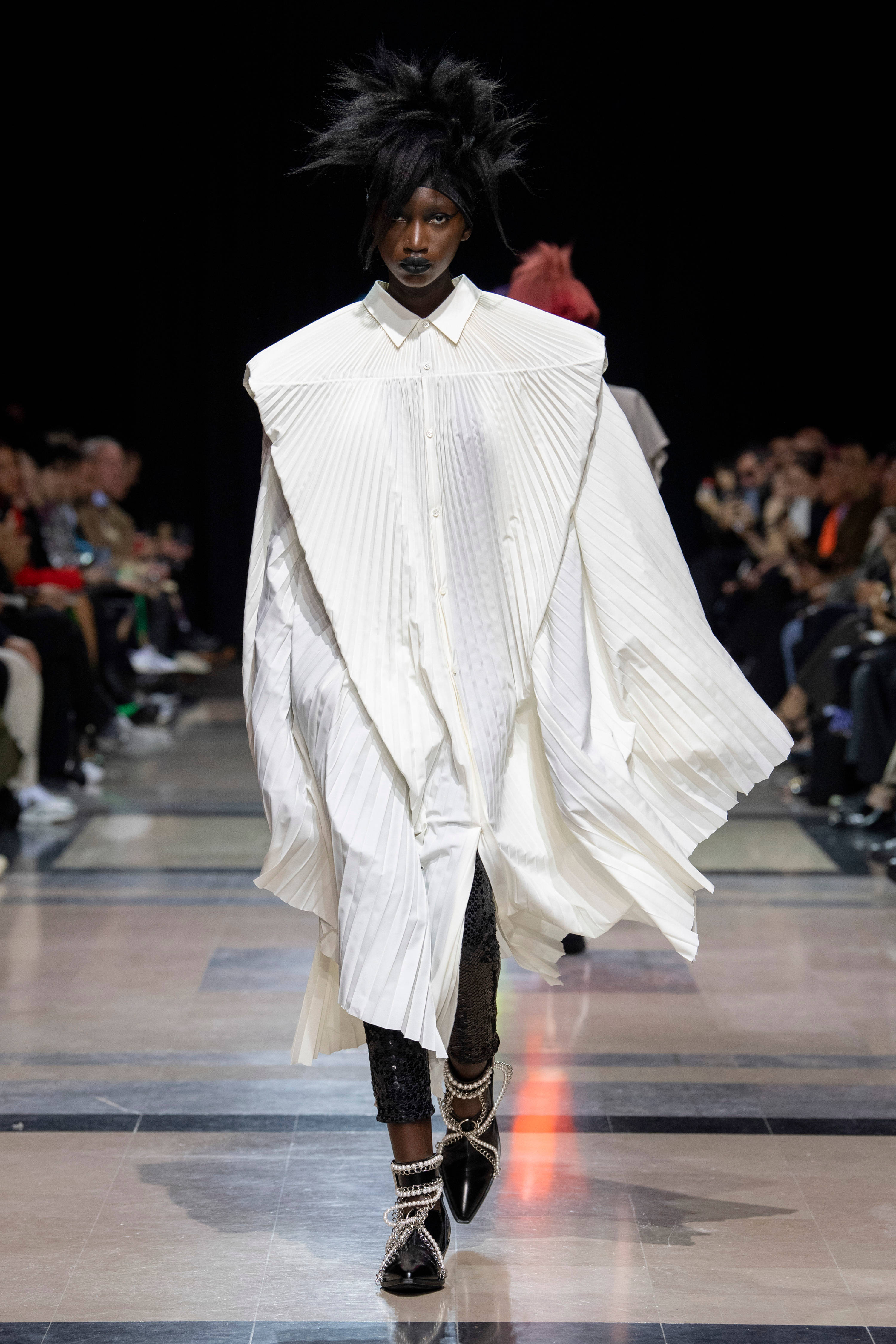 Comme Des Garçons 白色寬鬆連衣裙 壁紙 — 模特兒穿著戲劇性的超大白色褶襯衫裙，搭配尖刺黑髮和珍珠裝飾靴子走秀。