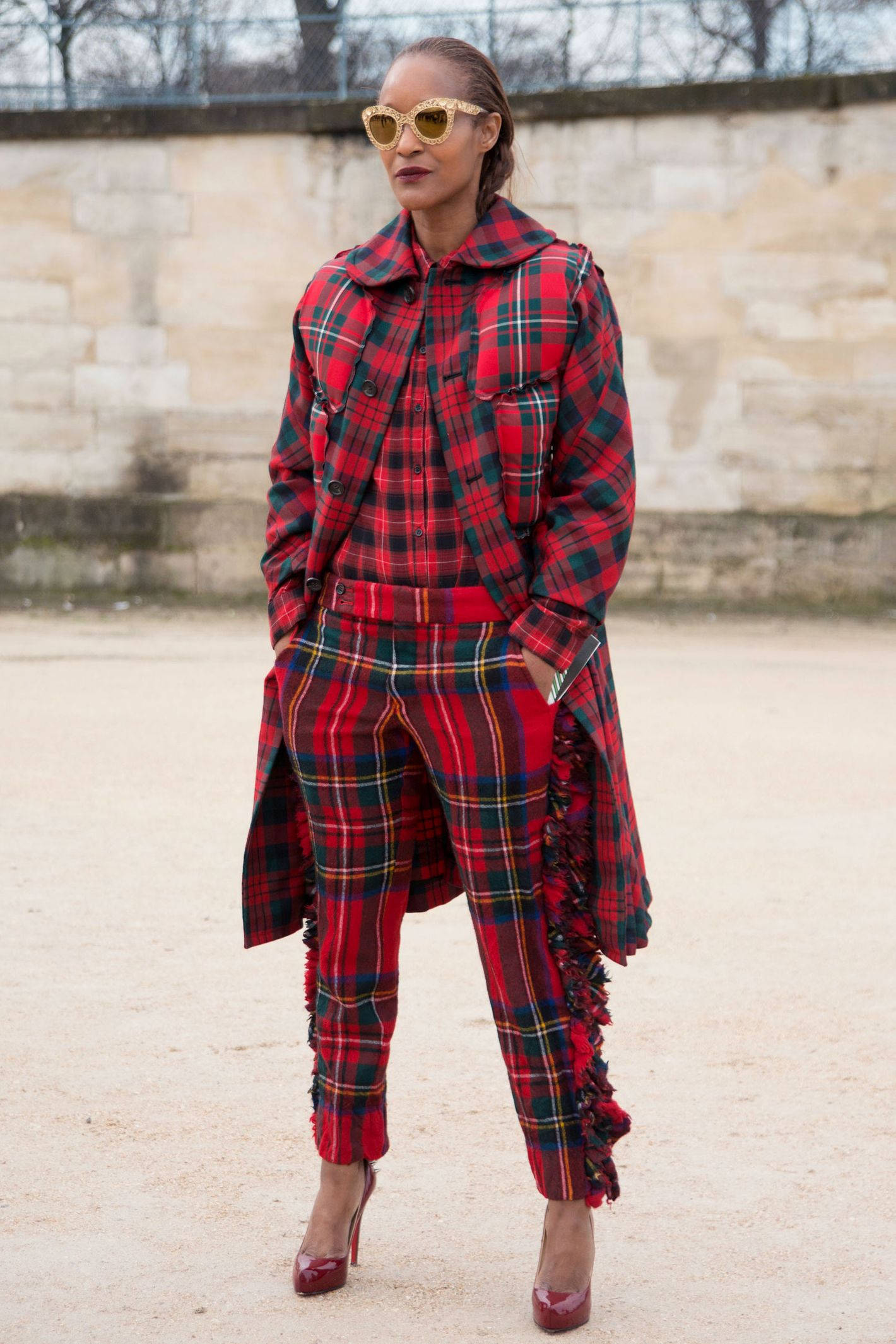 Comme Des Garçons紅黑格紋服裝 壁紙 — 一位時尚女性穿著大膽的紅色格紋外套和配套褲子，戴著金色太陽眼鏡和紅色高跟鞋，自信地站在戶外。