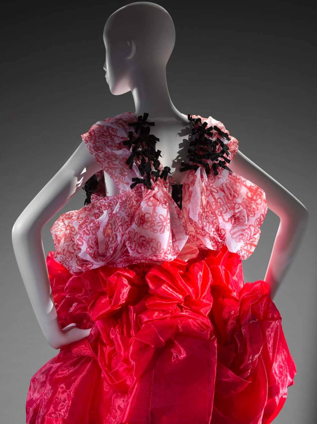 Comme Des Garçons紅色連衣裙人偶背影 壁紙 — 一個模特兒展示一件戲劇性的禮服，帶有紅色荷葉邊裙和飾有黑色蝴蝶結的圖案粉紅色緊身胸衣。