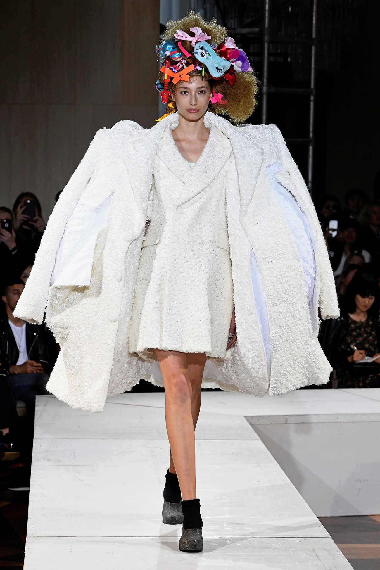 Comme Des Garçons 白色羊毛外套連衣裙 壁紙 — 一位模特兒穿著寬大的白色紋理外套和色彩繽紛的華麗頭飾走秀。