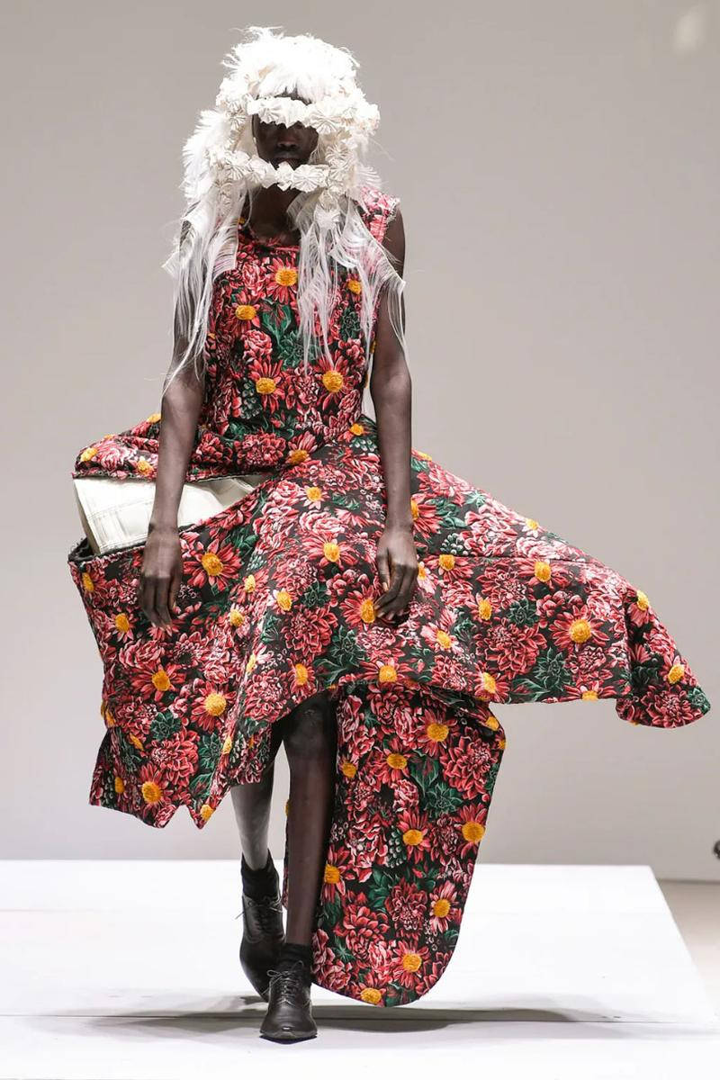 Comme Des Garçons 異形花朵連衣裙 壁紙 — 一位模特兒穿著大膽的花卉連衣裙和戲劇性的白色羽毛頭飾走秀。