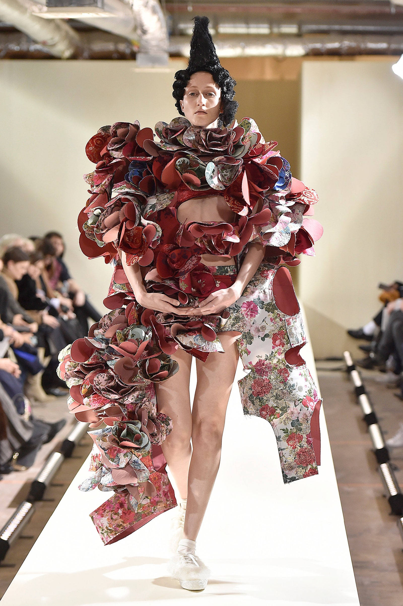 Comme Des Garçons 花紋前衛連衣裙 壁紙 — 一位模特兒穿著由層疊紅色花卉布料和高黑色帽子組成的前衛服裝走在天橋上。