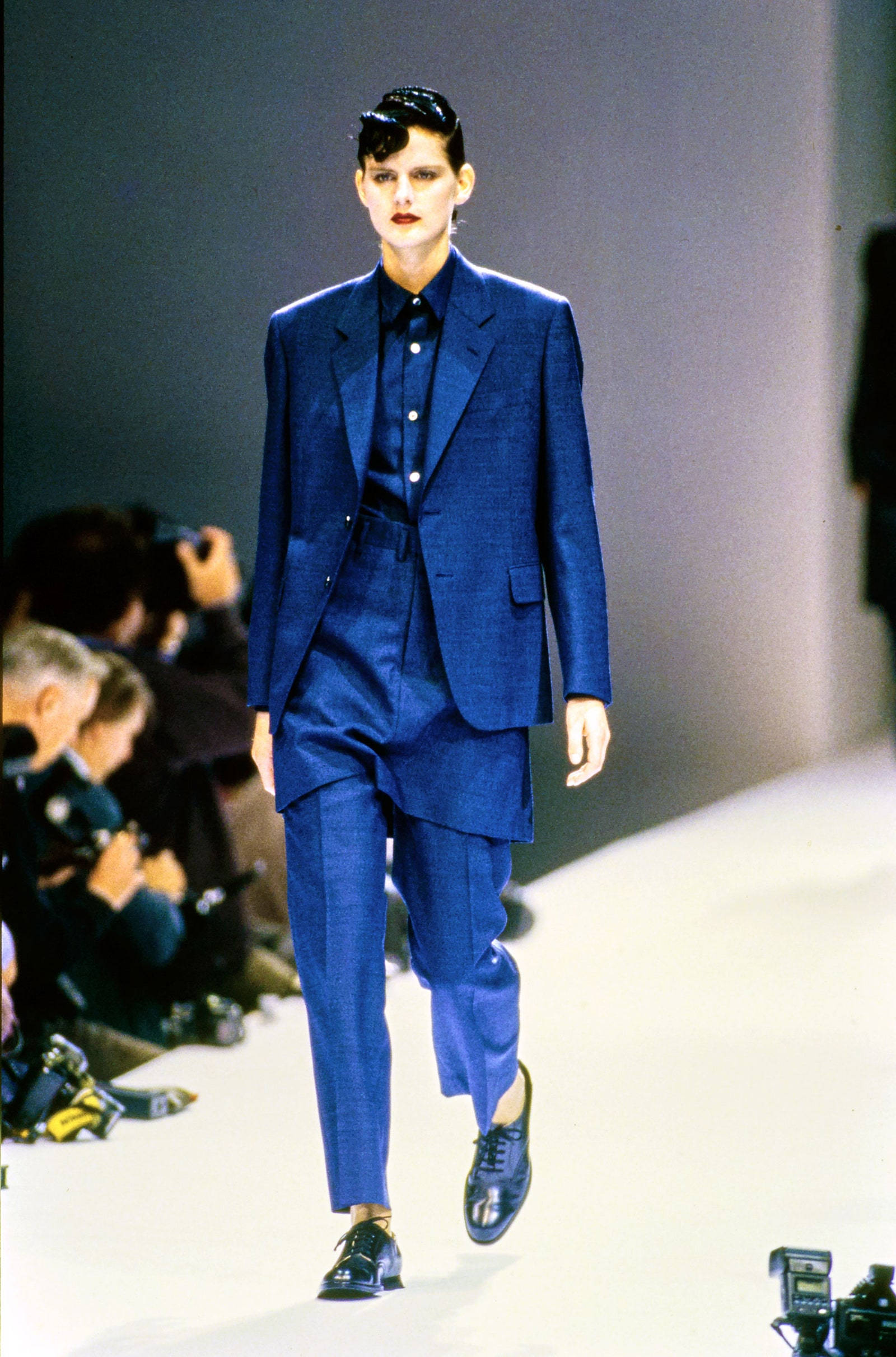 Comme Des Garçons 藍色正裝 壁紙 — 一位模特兒在明亮的燈光下，自信地穿著訂製的鈷藍色西裝走在時裝天橋上。