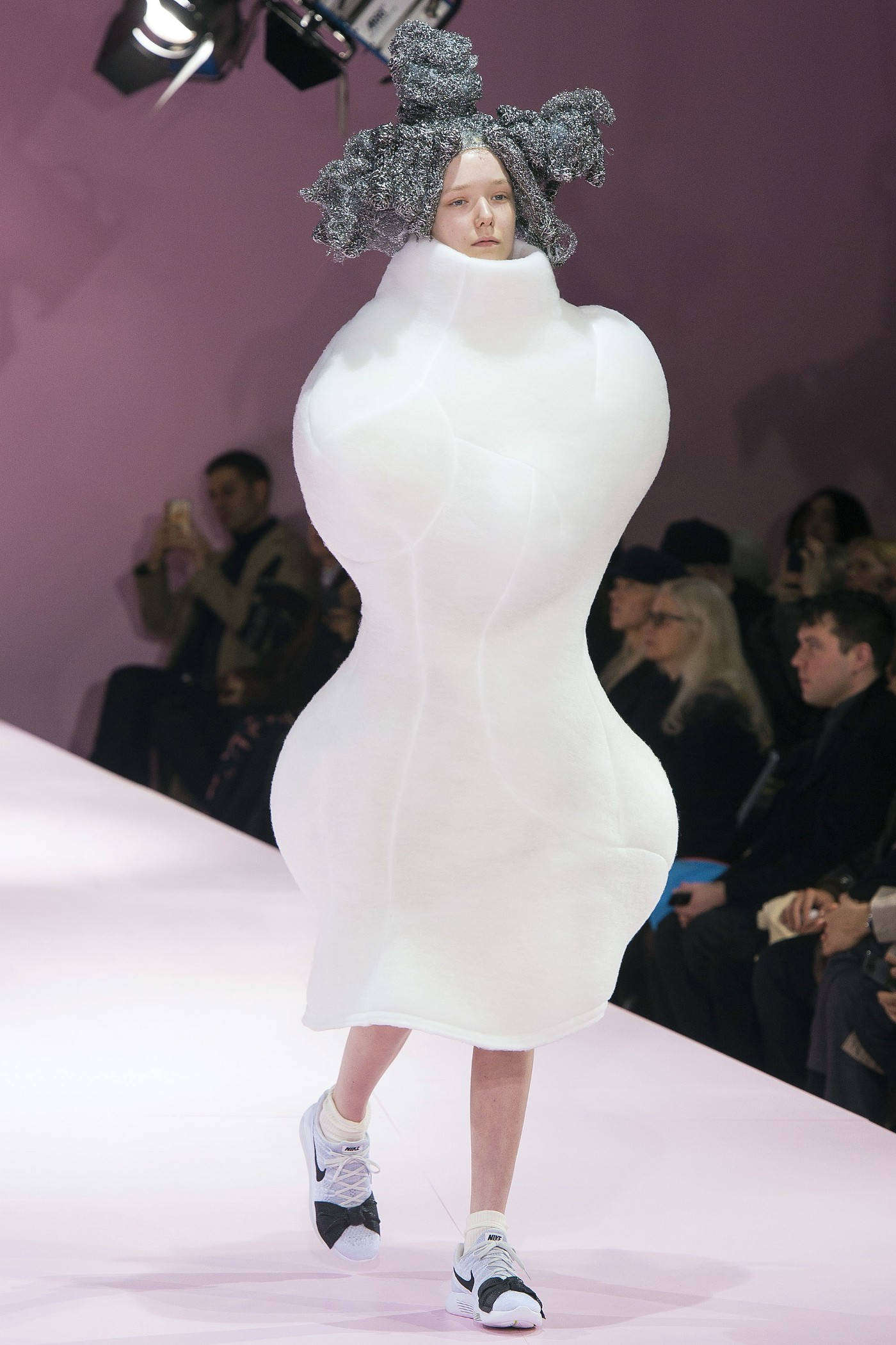 Comme Des Garçons 前衛瓶型長裙 壁紙 — 一位模特兒在粉紅色天橋上走秀，身穿雕塑般的白色連衣裙和銀色頭飾，同時穿著運動鞋。