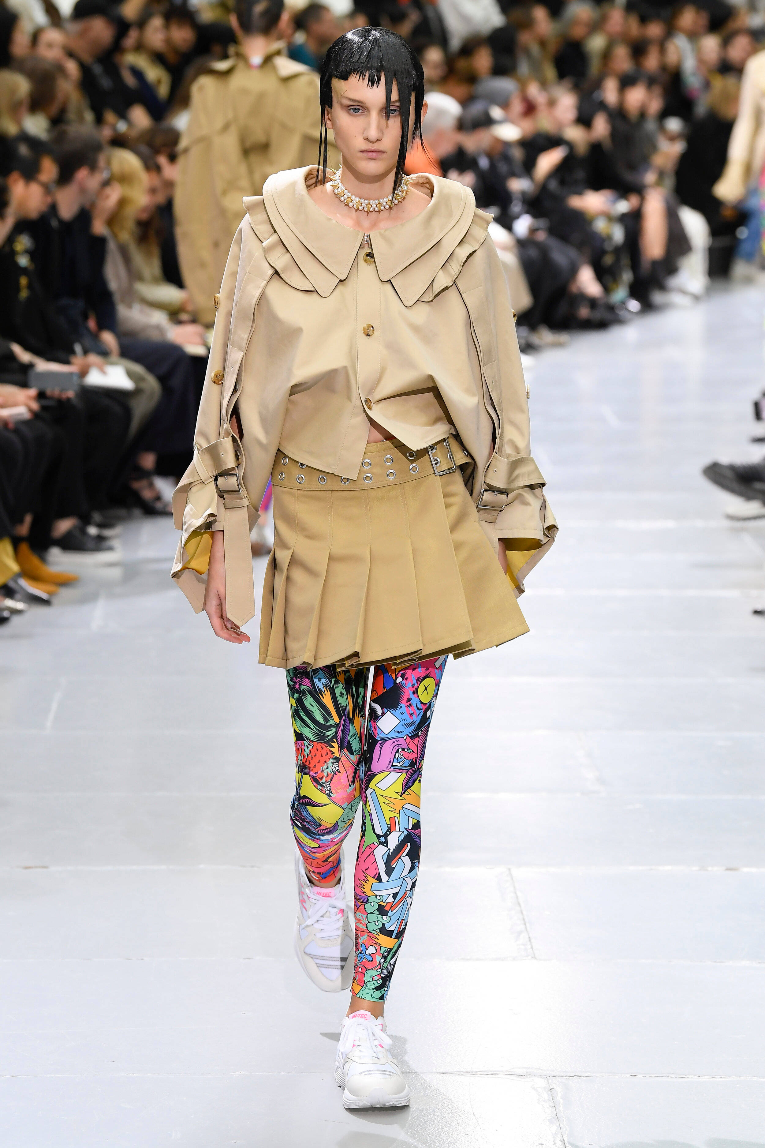 Comme Des Garçons 咖啡色上衣與裙裝 壁紙 — 一位模特兒穿著米色寬鬆外套和充滿活力的塗鴉風格緊身褲走在天橋上。