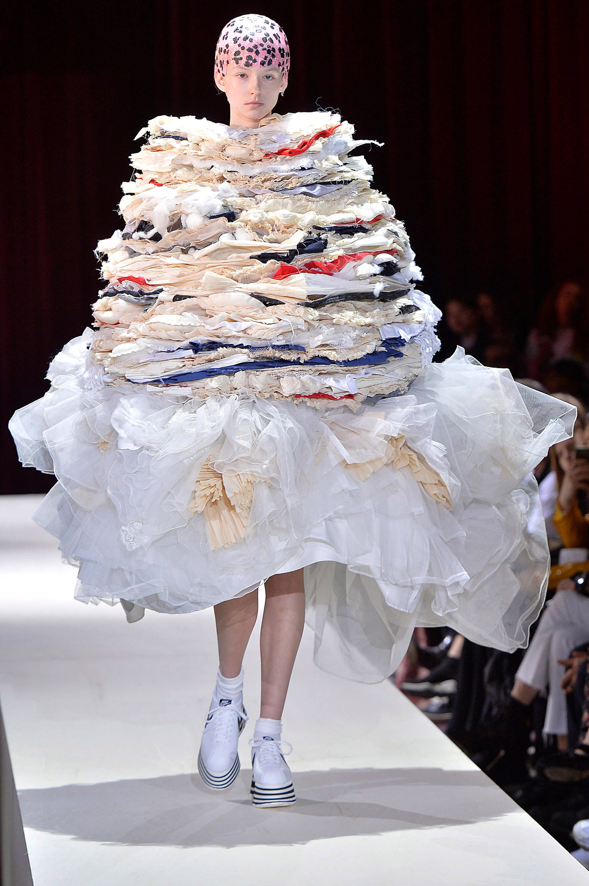 Comme Des Garçons 巨大荷葉邊連衣裙 壁紙 — 一位模特兒穿著由堆疊布料碎片和白色薄紗裙製成的前衛服裝走秀。