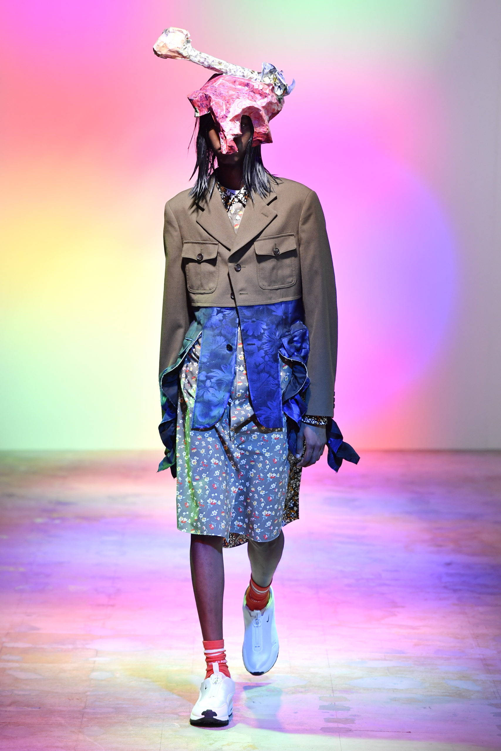 Comme Des Garçons 多層次服裝 壁紙 — 模特兒在充滿活力的彩虹燈光下，穿著超現實服裝，戴著骨頭形狀的頭飾走秀。