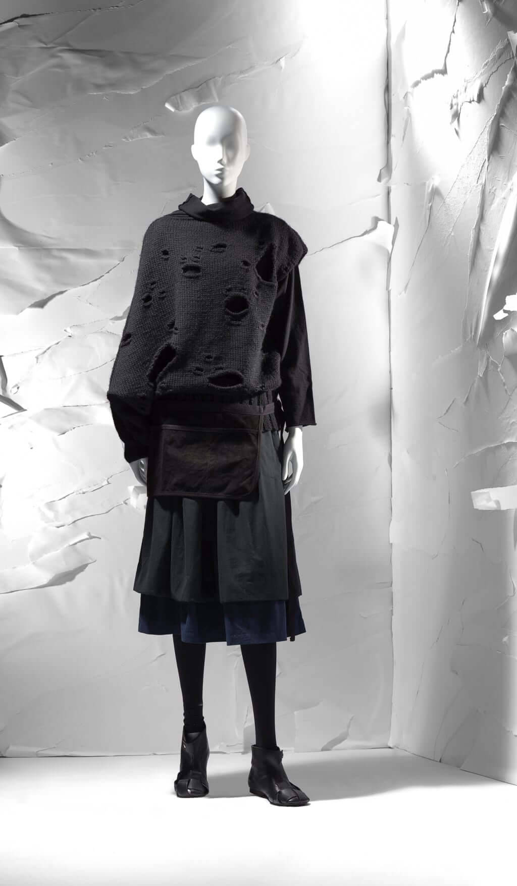 Comme Des Garçons黑色長袖上衣 壁紙 — 一個模特兒穿著破舊的黑色針織上衣和分層裙子，背景是帶有紋理的白色背景。