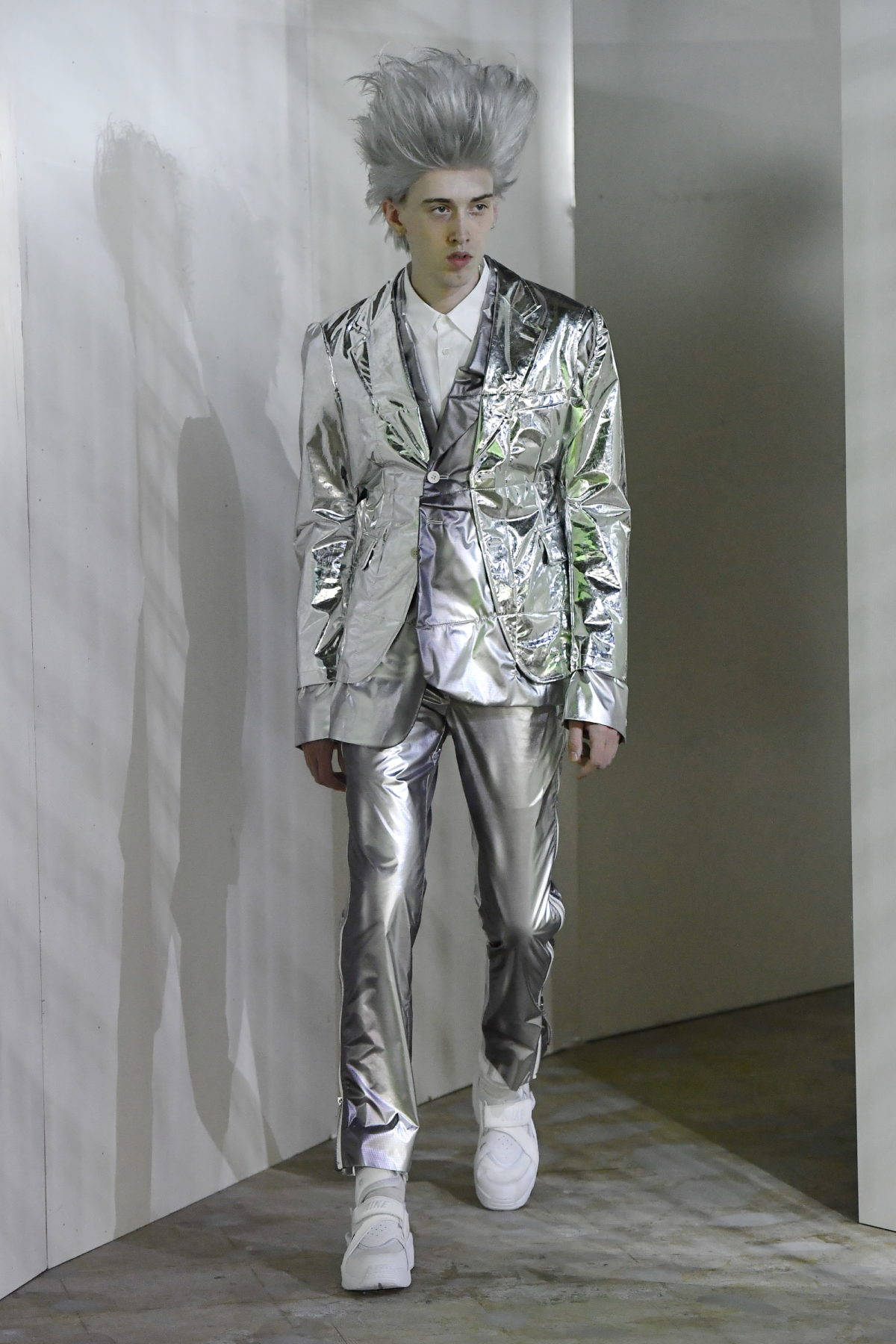Comme Des Garçons銀色未來感服裝 壁紙 — 一位銀色尖刺頭髮的模特兒，穿著全套銀色金屬套裝和白色運動鞋，站在純白牆壁前。