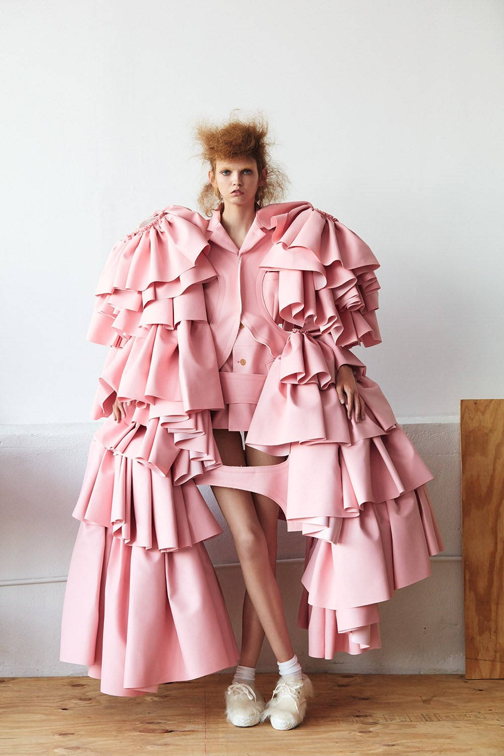 Comme Des Garçons 粉紅荷葉邊連衣裙 壁紙 — 模特兒穿著前衛的粉紅色荷葉邊服裝，在極簡白色牆壁和木地板上展現戲劇性的體積感。