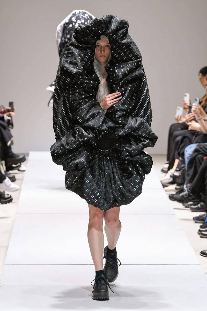 Comme Des Garçons 2023春夏時裝秀 壁紙 — 模特兒穿著前衛黑色紋理服裝，搭配超大荷葉邊袖子和戲劇性連帽，在時裝展上走秀。