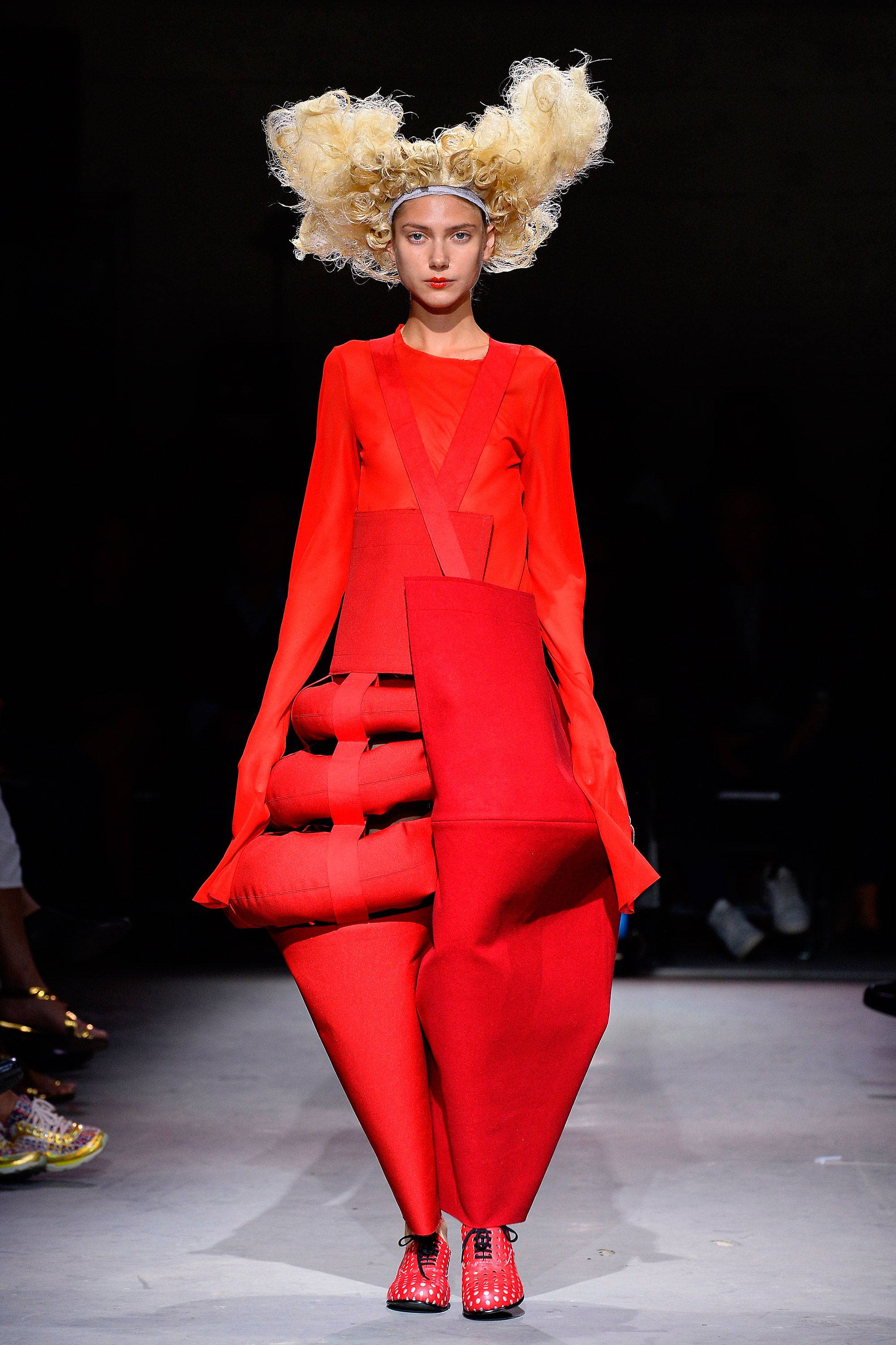 Comme Des Garçons 紅色不規則剪裁連身裝 壁紙 — 一位模特兒穿著大膽的紅色前衛服裝，搭配豐盈雕塑般的髮型和相配的鞋子，走在天橋上。
