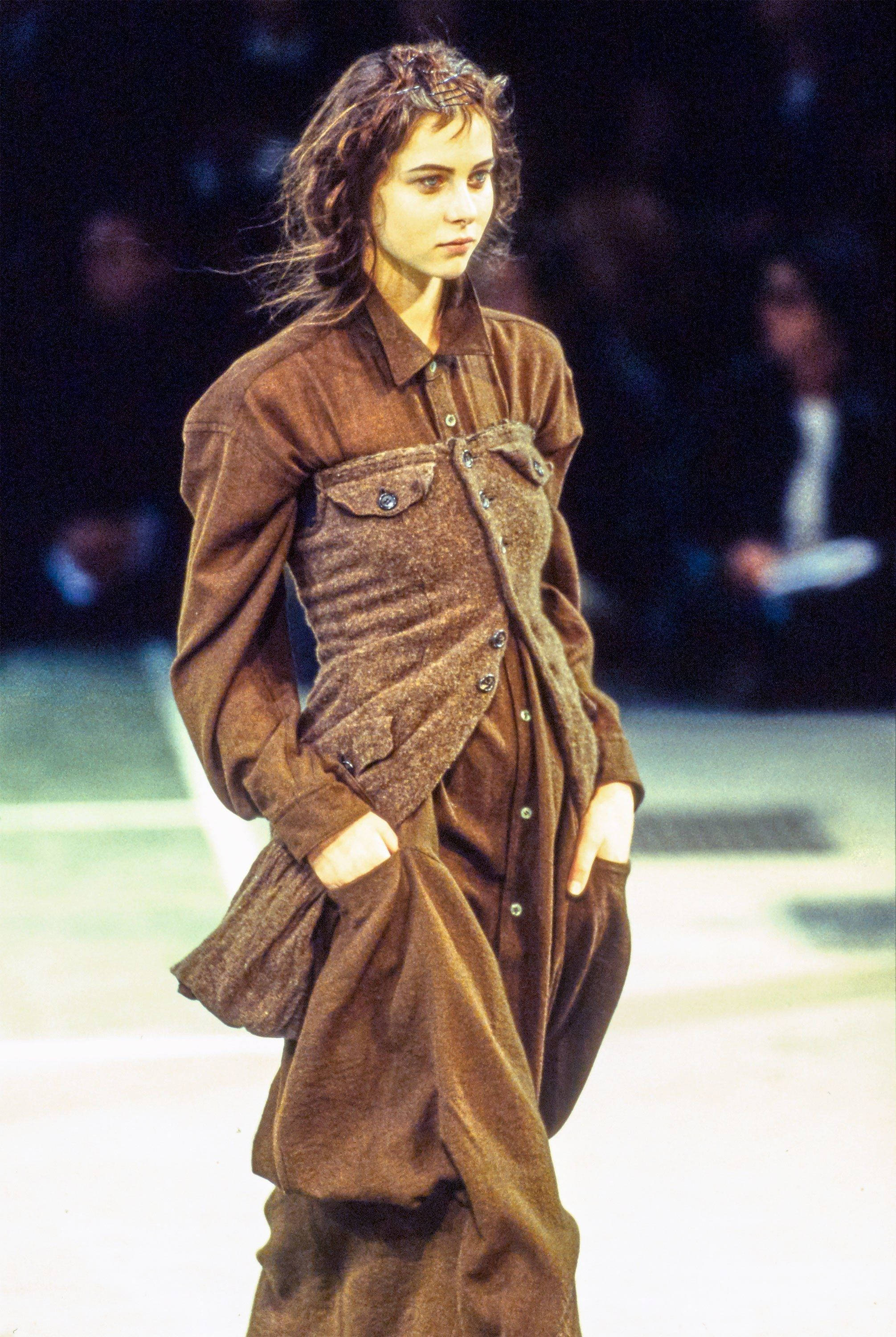 Comme Des Garçons 長棕色襯衫裙 壁紙 — 模特兒在明亮的舞台燈光下，穿著質感豐富的棕色分層服裝走秀。