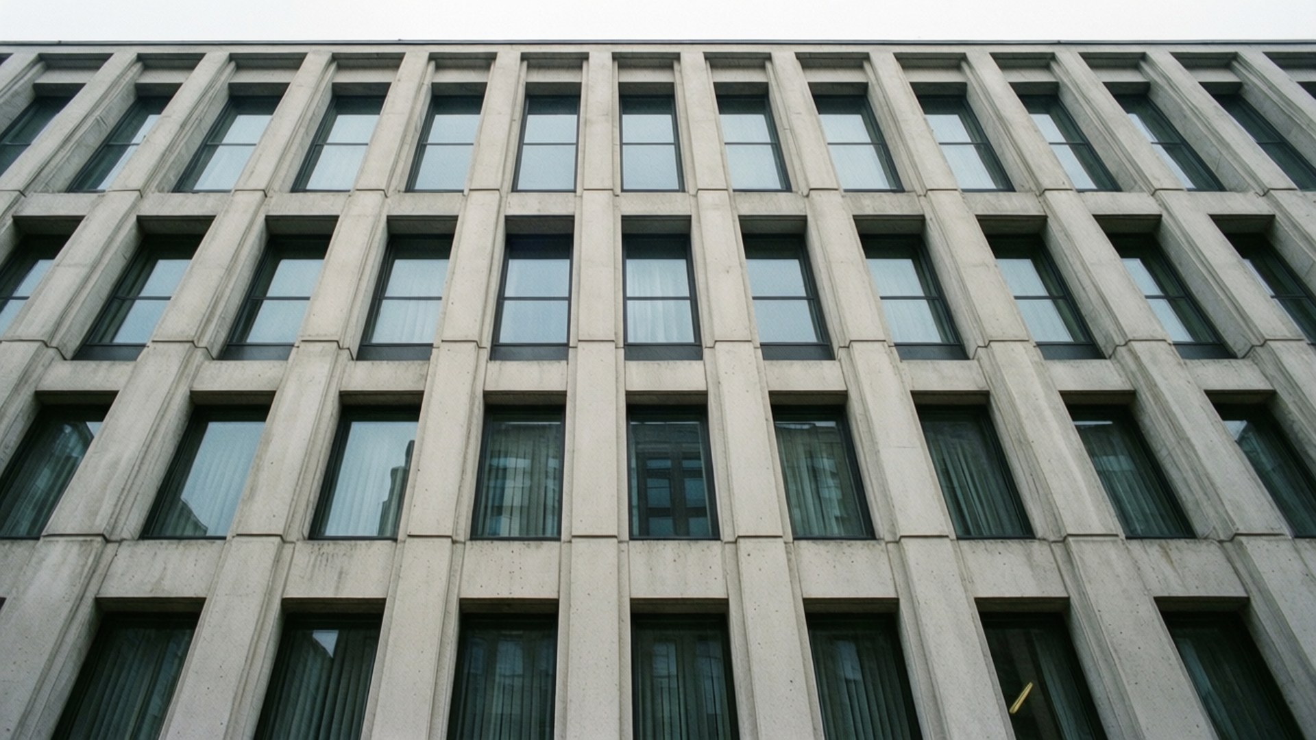 Concrete Facade Windows 壁紙 — 灰色混凝土建築的低角度視圖，帶有重複的矩形窗戶和深色窗簾。