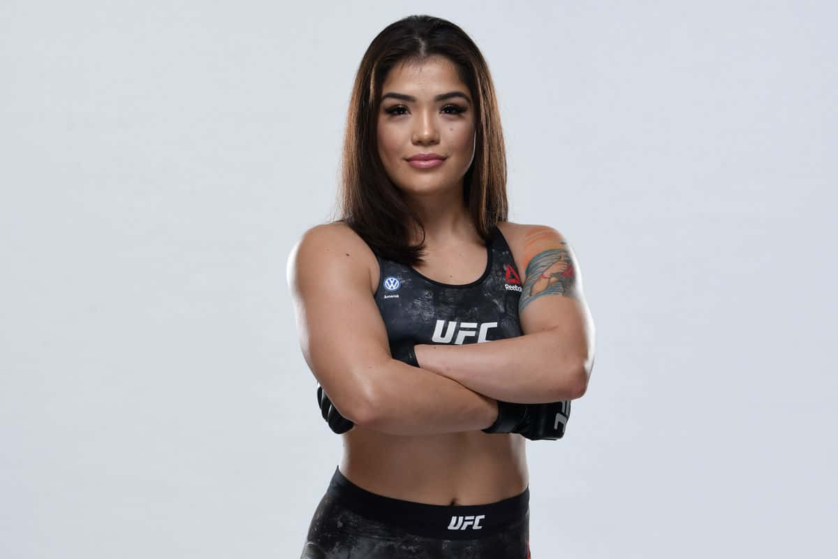  壁紙 — 一位自信嘅女性UFC拳手交叉雙臂，身穿品牌運動裝備，企喺純色嘅工作室背景前。