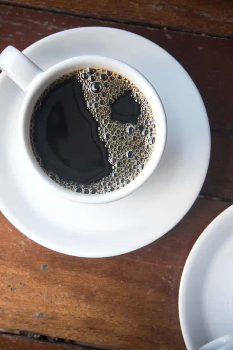  壁紙 — 從上方俯瞰一個白色咖啡杯，裡面裝著深色咖啡和泡沫，放在質樸的木桌上。