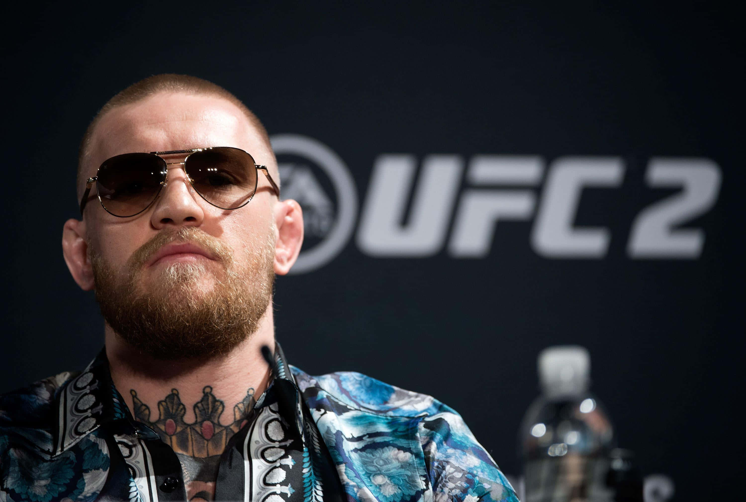康納·麥格雷戈 桌布 壁紙 — Conor McGregor 喺 UFC 2 記者會上戴住飛行員太陽眼鏡同圖案恤衫，背景係黑色。