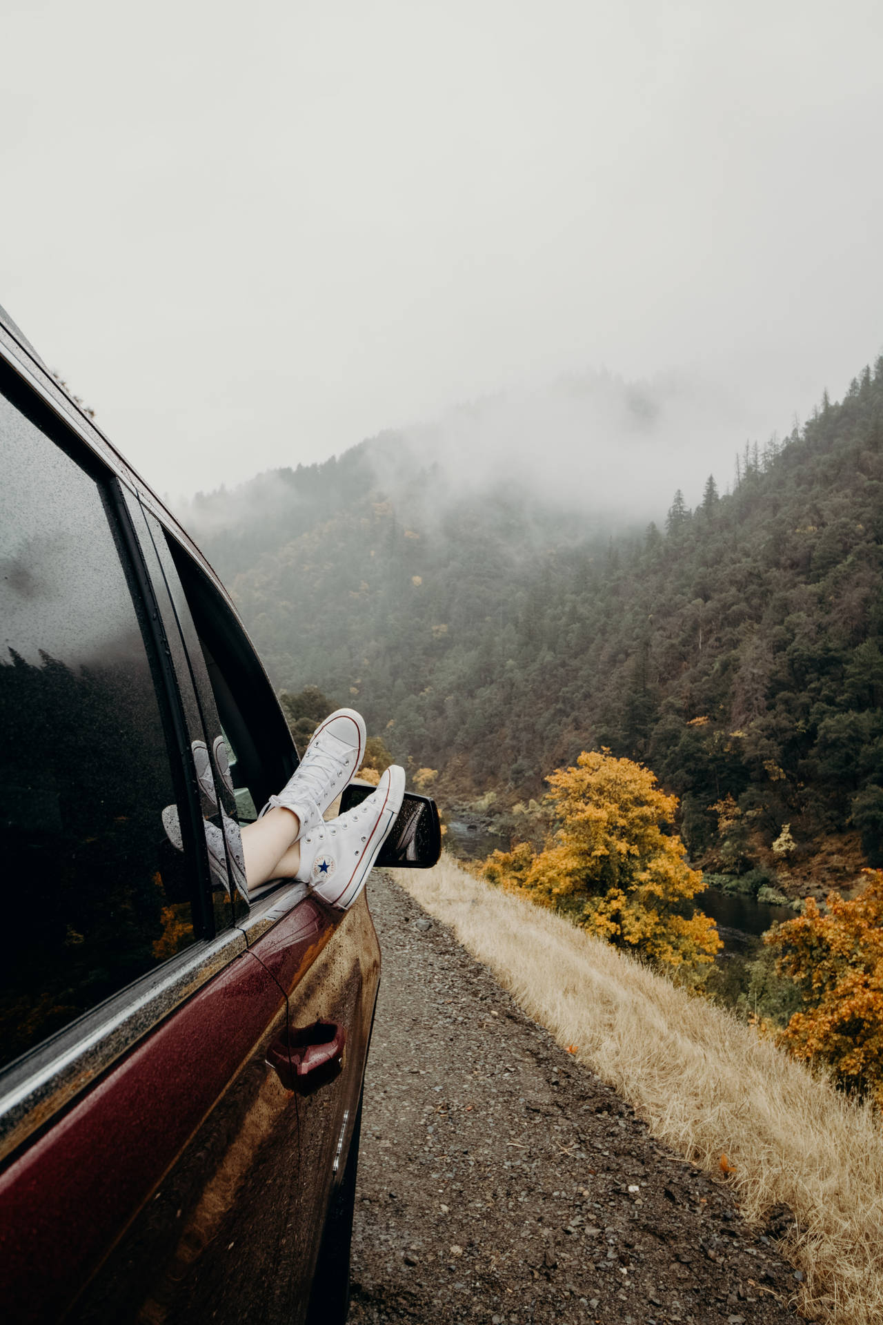 穿著白色運動鞋的腳從霧氣瀰漫的山路上的車窗伸出。