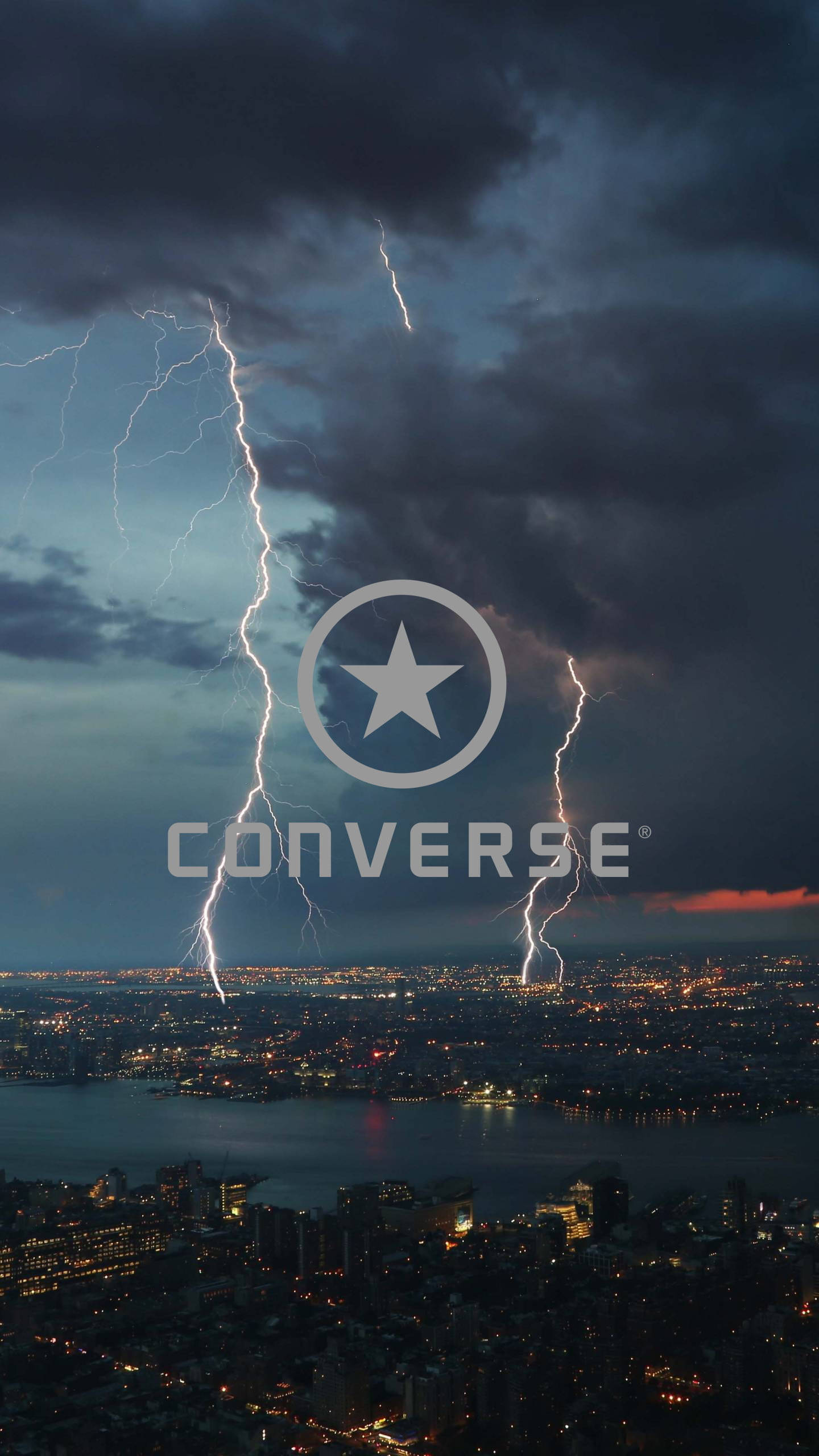Converse 標誌城市閃電 壁紙 — 閃電照亮暴風雨的天空，下方是夜晚中燈火輝煌的廣闊城市景觀。