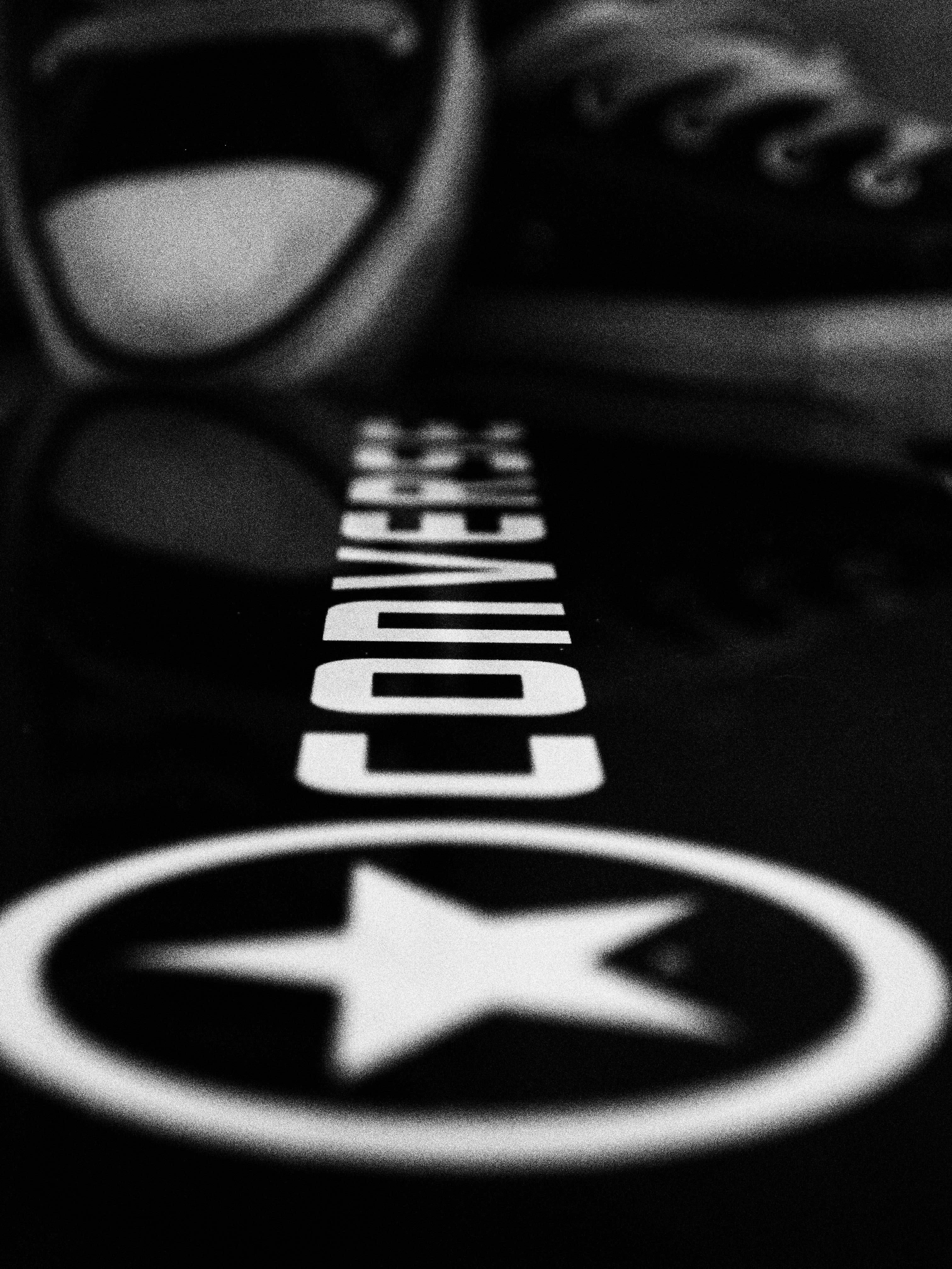 Converse 標誌透視拍攝 壁紙 — 黑白特寫，Converse 運動鞋標誌投射在反光表面上，背景有模糊的鞋子。