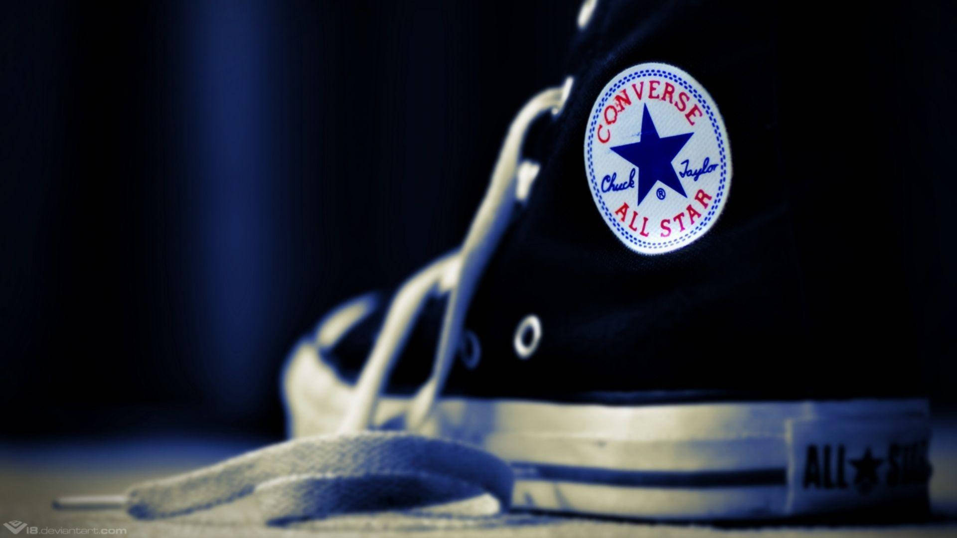 Converse 標誌運動鞋 壁紙 — 黑色Converse Chuck Taylor All Star運動鞋的特寫，白色鞋帶和鞋底，在深色背景下沐浴在冷藍色光中。