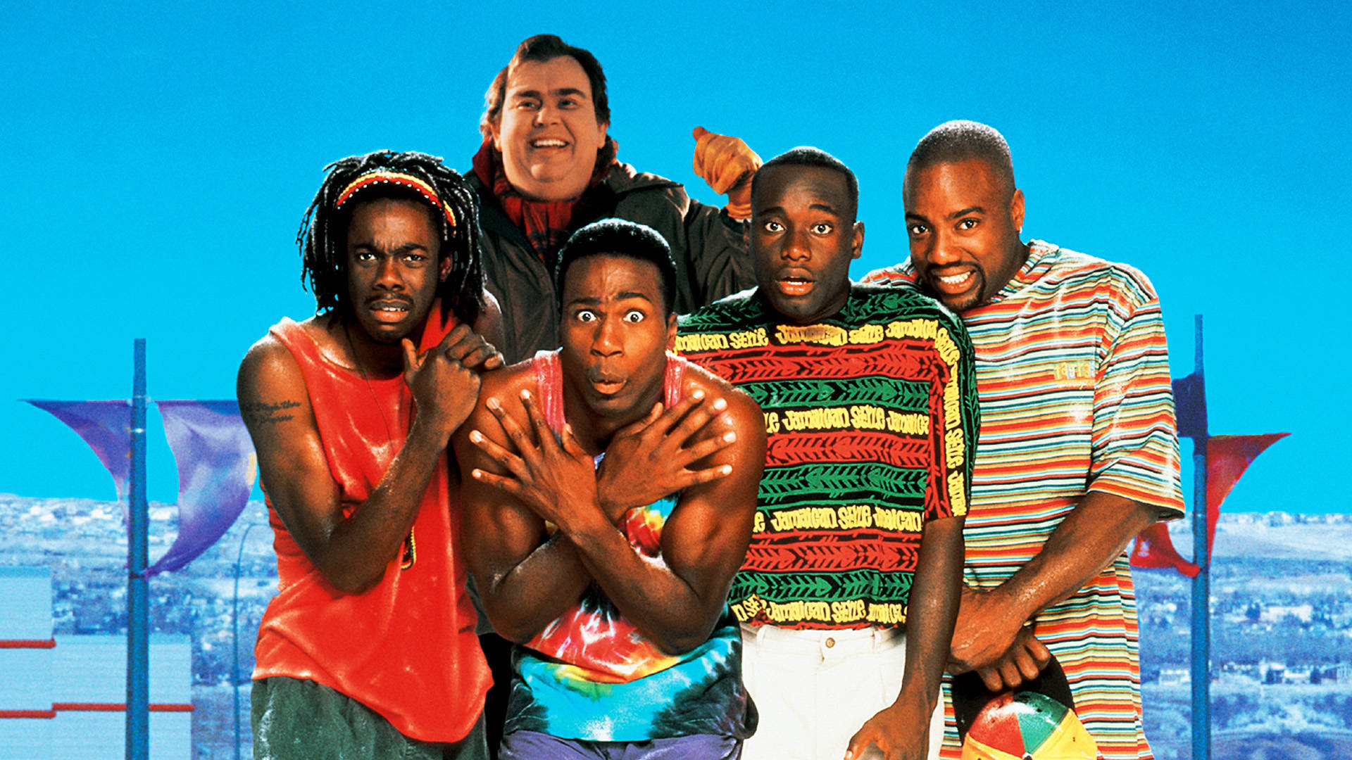 《Cool Runnings》約翰·坎迪 壁紙 — 五個穿著色彩繽紛90年代街頭服飾的男人，在明亮的藍天和城市景觀前擺出誇張的表情。