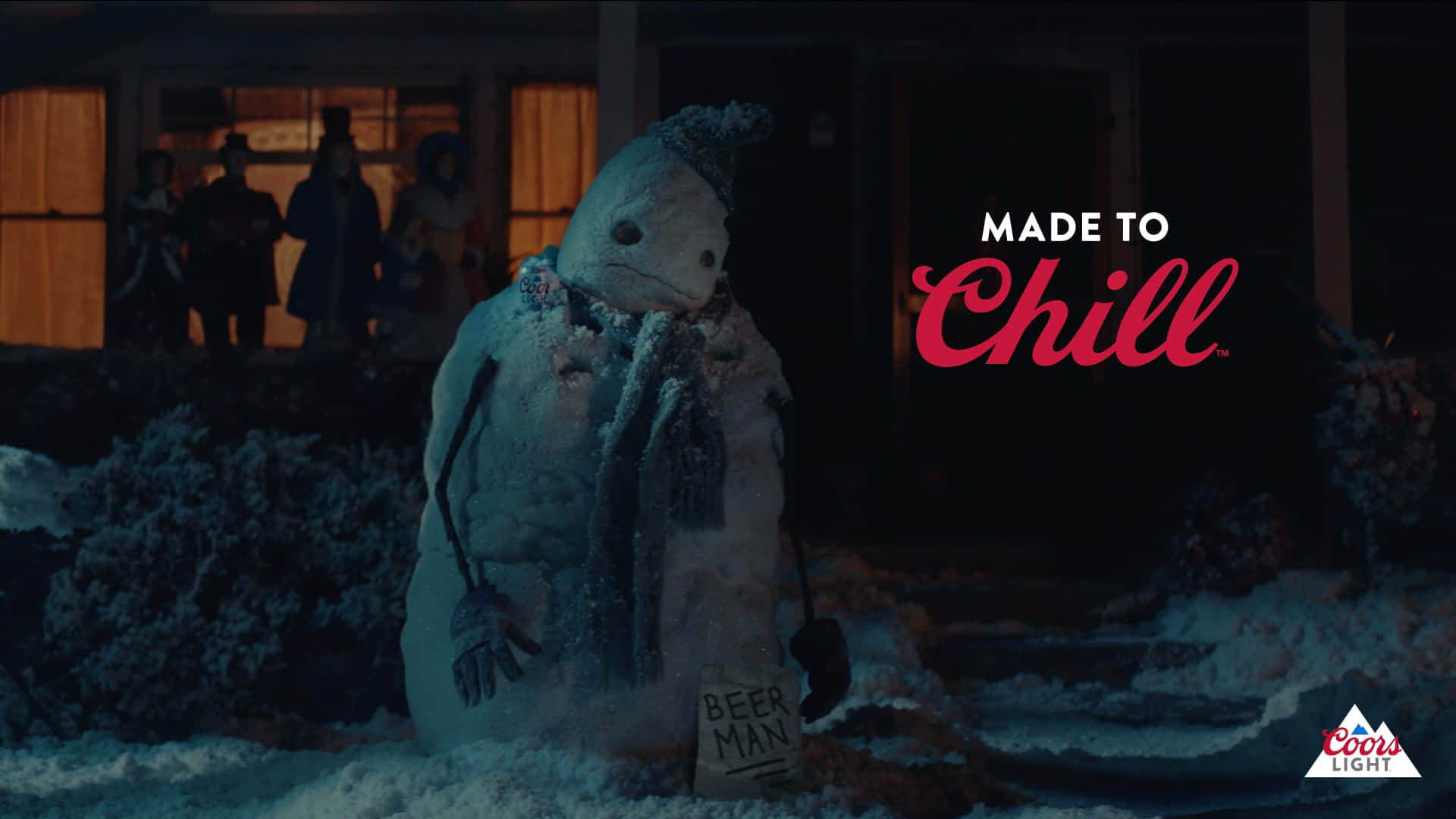 Coors Light 廣告場景 壁紙 — 一個戴著圍巾、舉著寫有「BEER MAN」牌子的雪人，夜晚站在一間溫暖燈光的房子前。