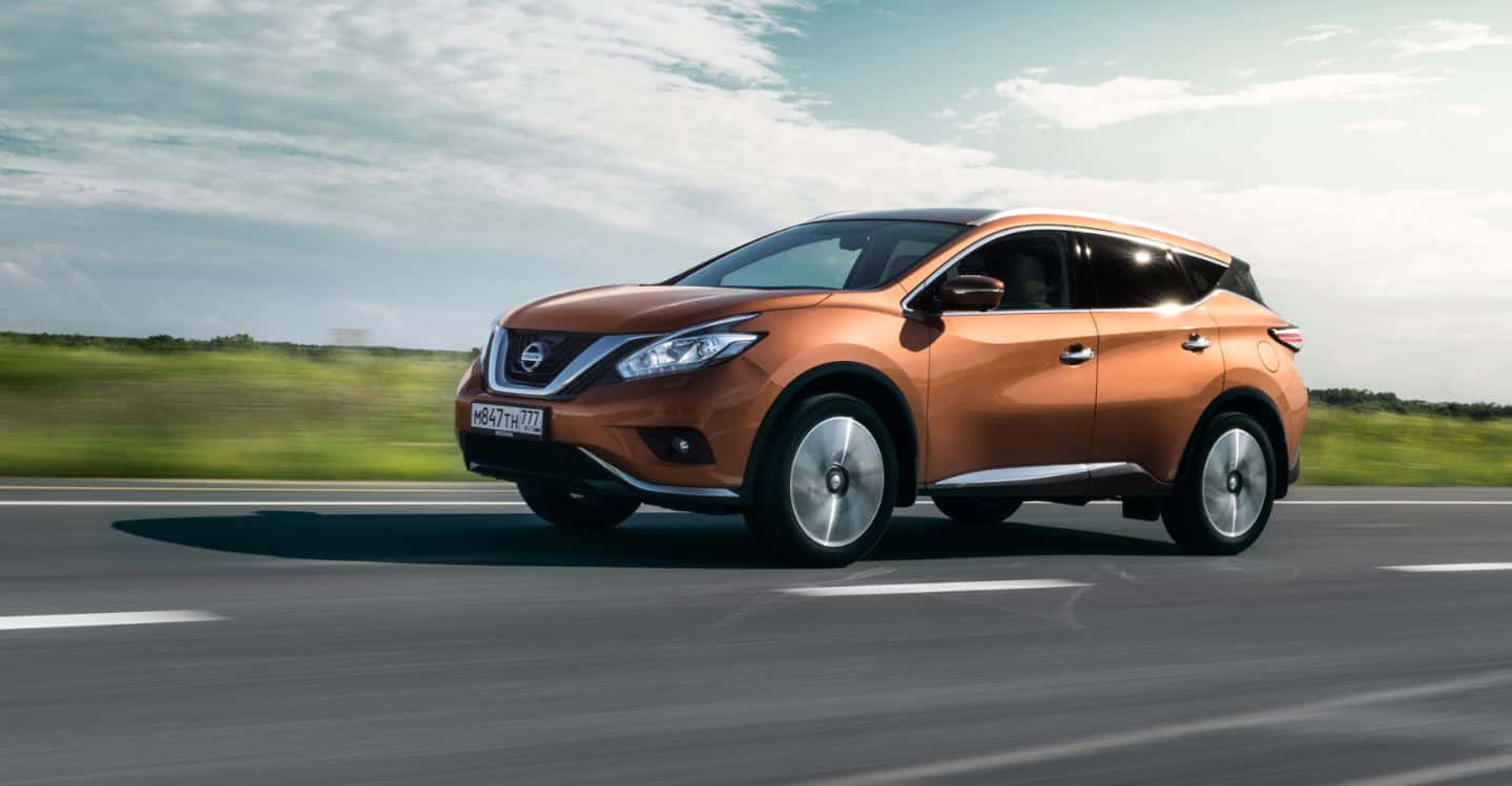 Nissan Murano 桌布 壁紙 — 一輛銅色的日產Murano SUV在部分多雲的天空下，沿著高速公路疾馳，背景是模糊的綠色田野。