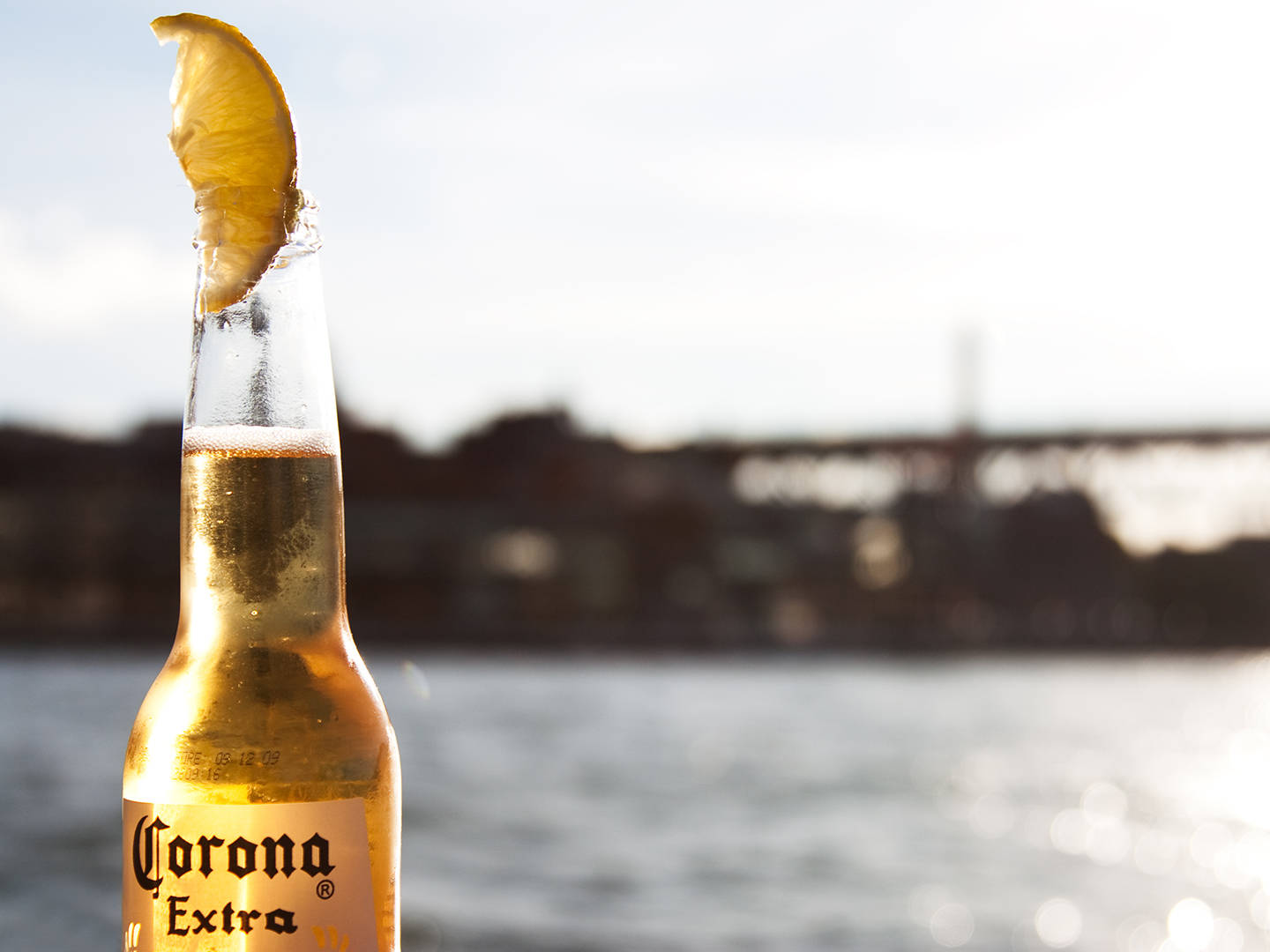 與Corona Extra一同逃離喧囂，尋找寧靜 壁紙 — 一支冰凍的Corona Extra啤酒瓶配上青檸角，在日落時分的水邊閃閃發光。