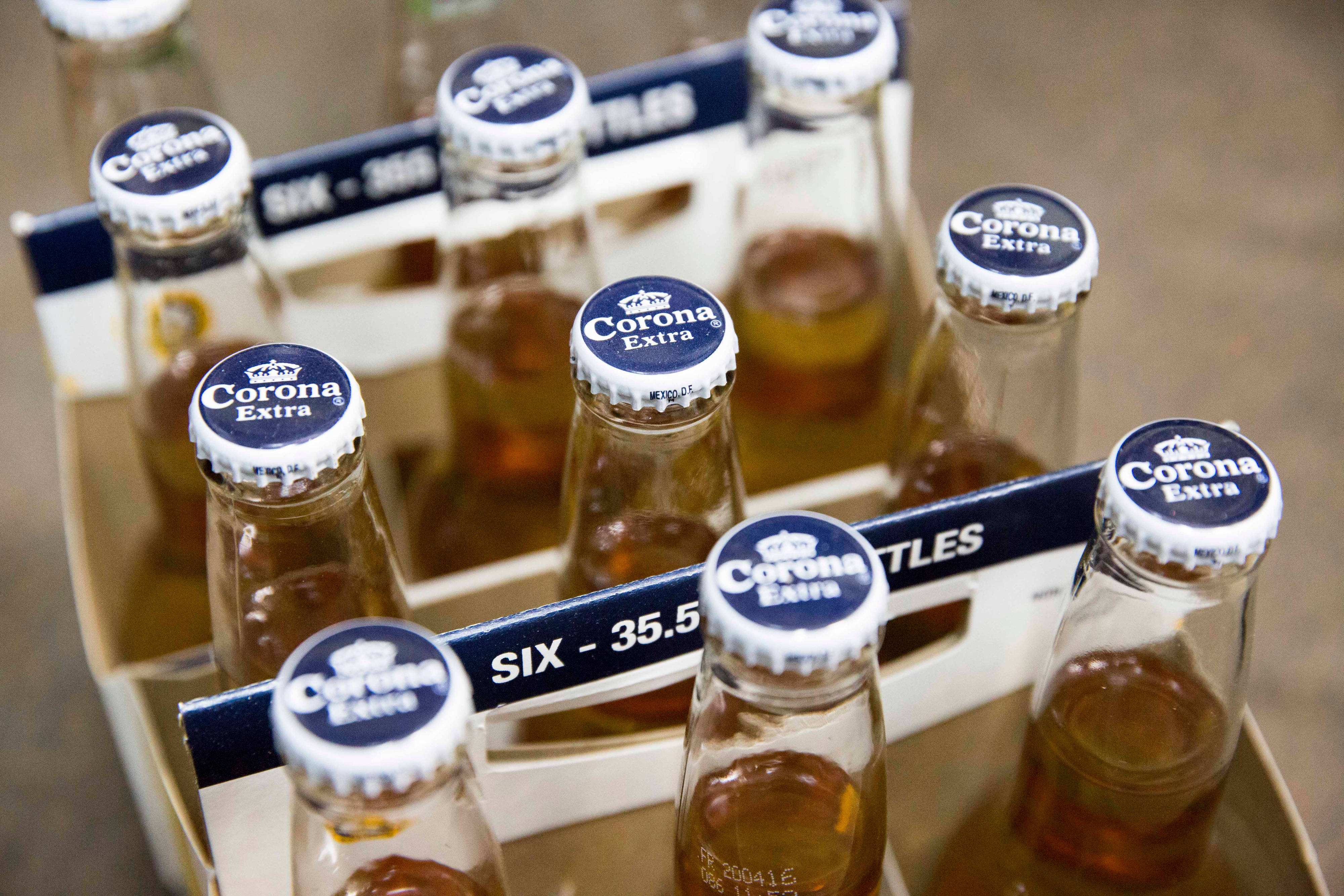 Corona Extra啤酒包裝盒視角 壁紙 — 六瓶Corona Extra啤酒裝在紙板提架中的特寫，金色液體透過玻璃可見。